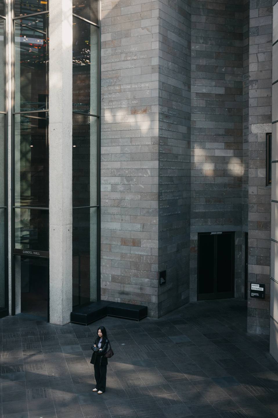 A solitary figure between tall stone and glass walls.
