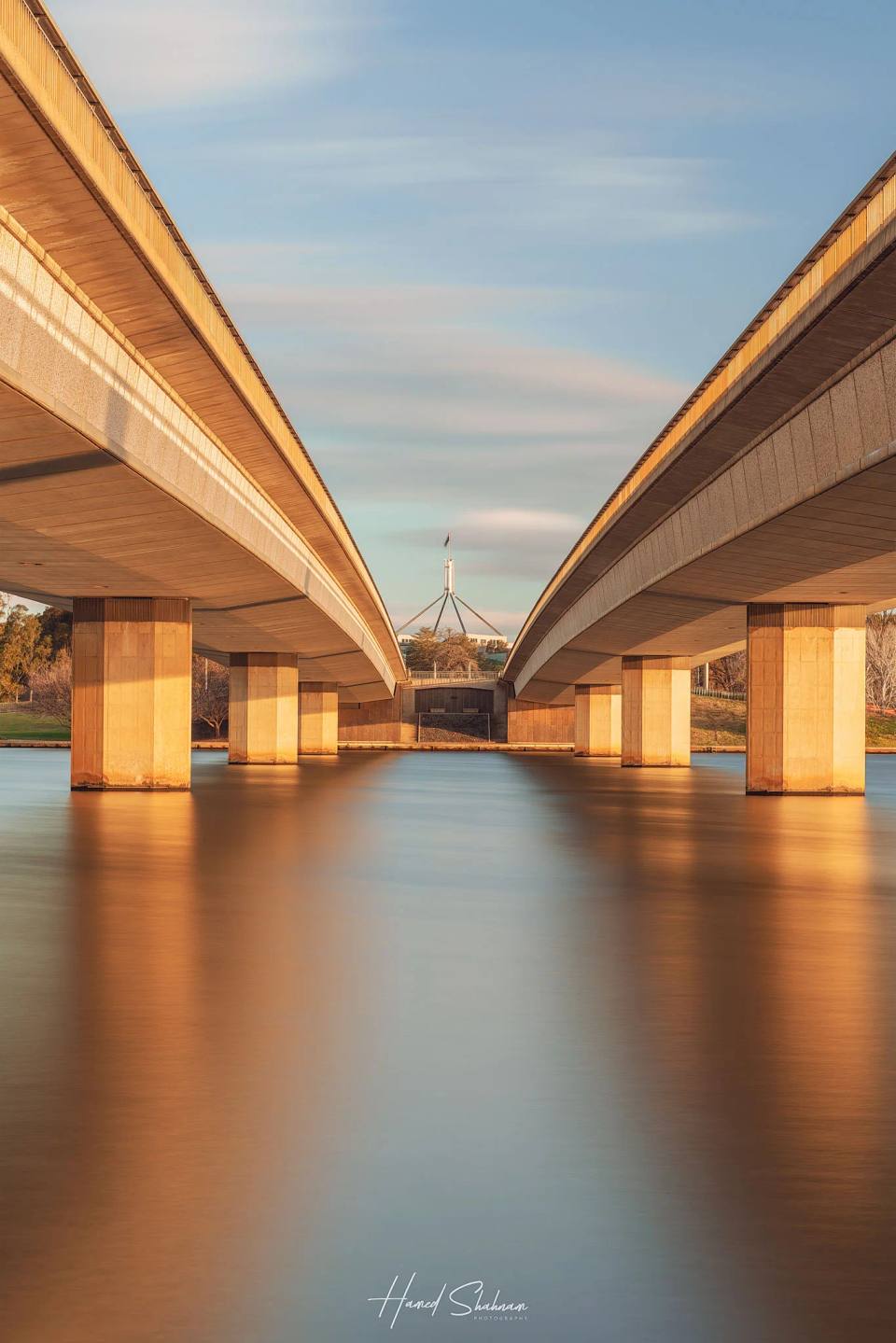 Warm light beneath Commonwealth Bridge reflected in smooth lake water.