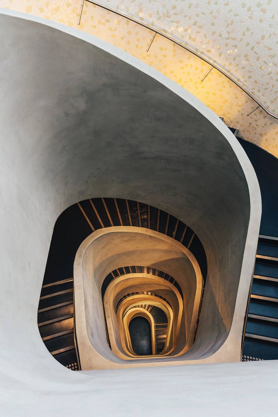 A view through repeating curved stairwells and timber handrails.
