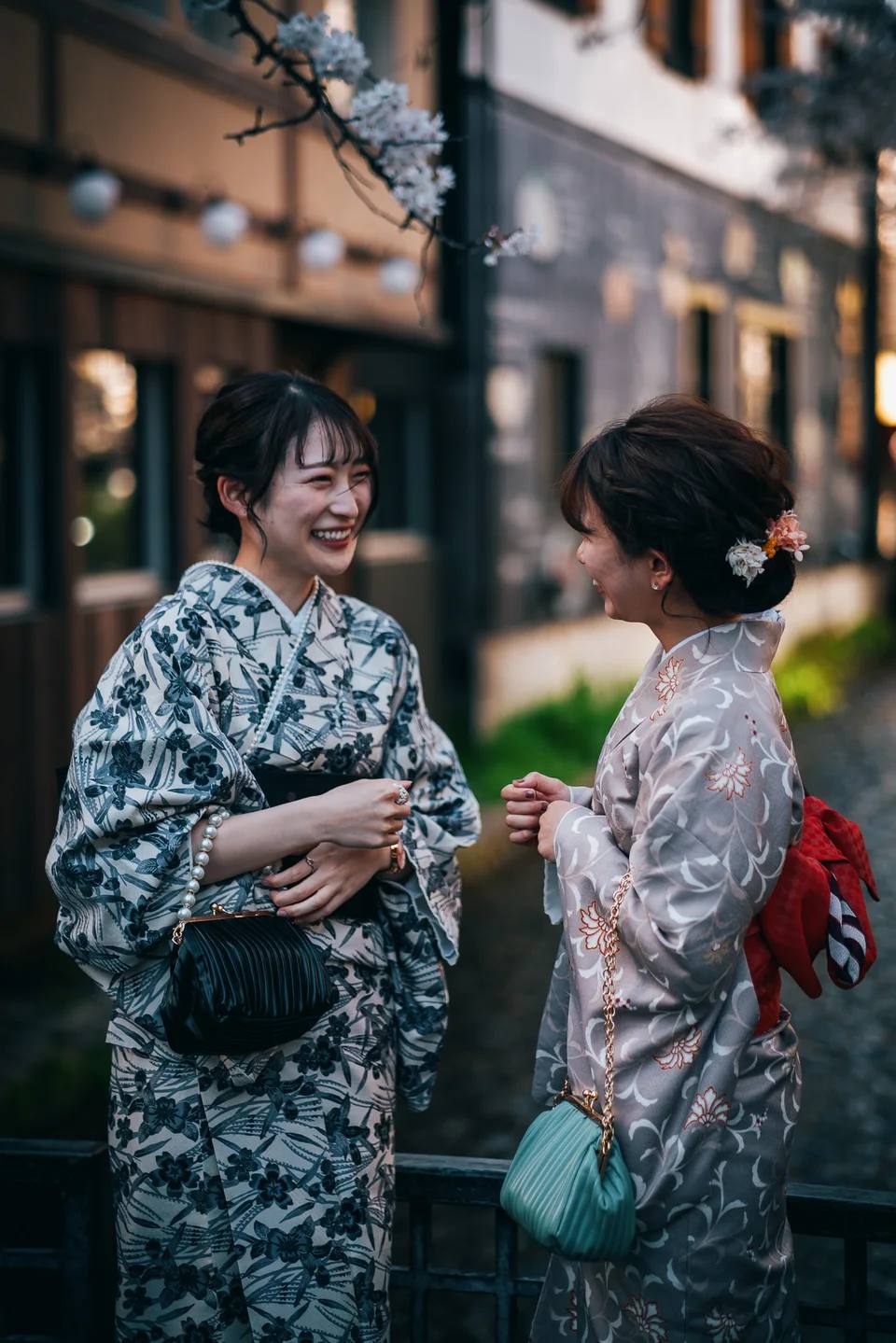 Two people in kimono talking beside a traditional street.