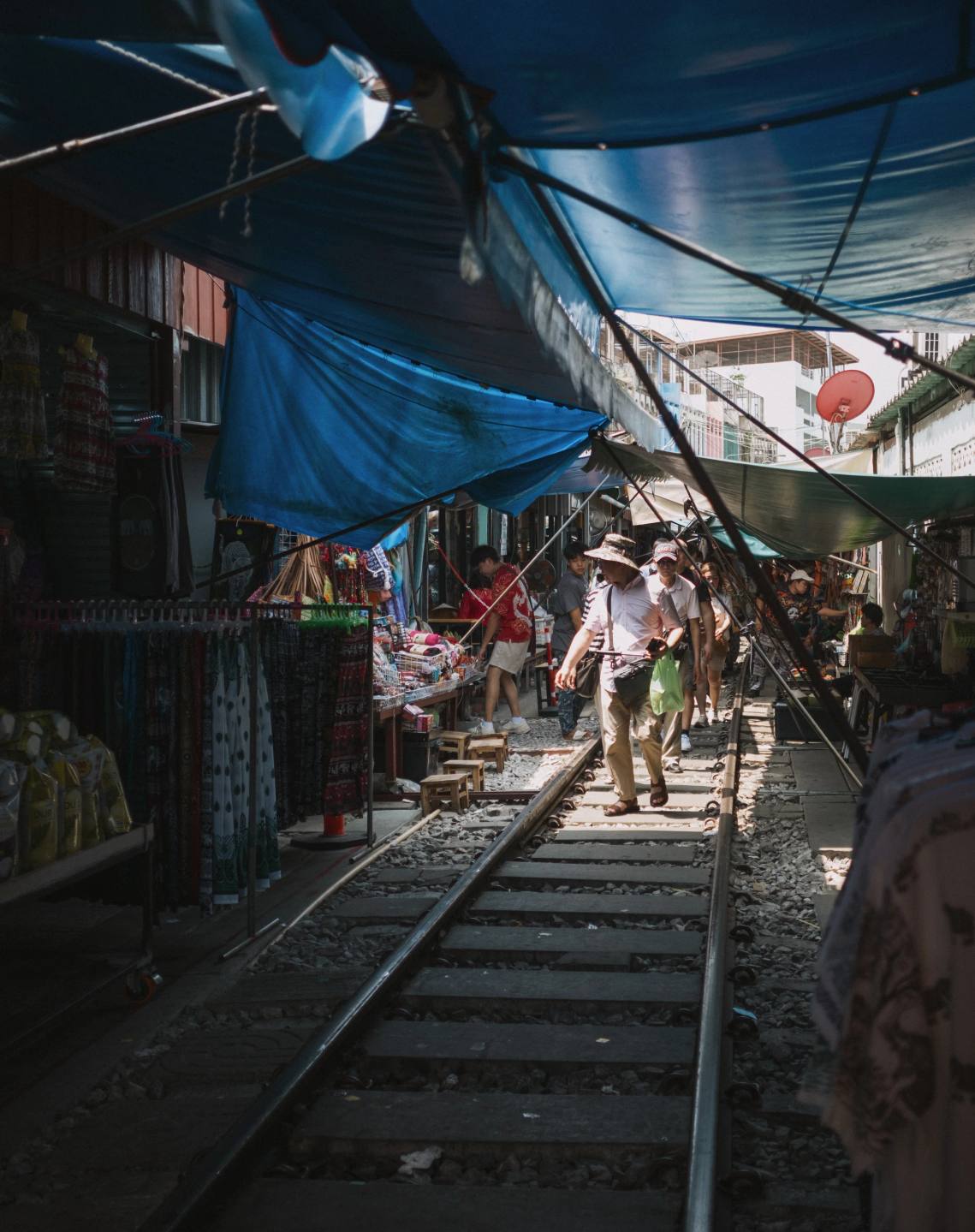 Railway tracks running through a market under blue awnings.