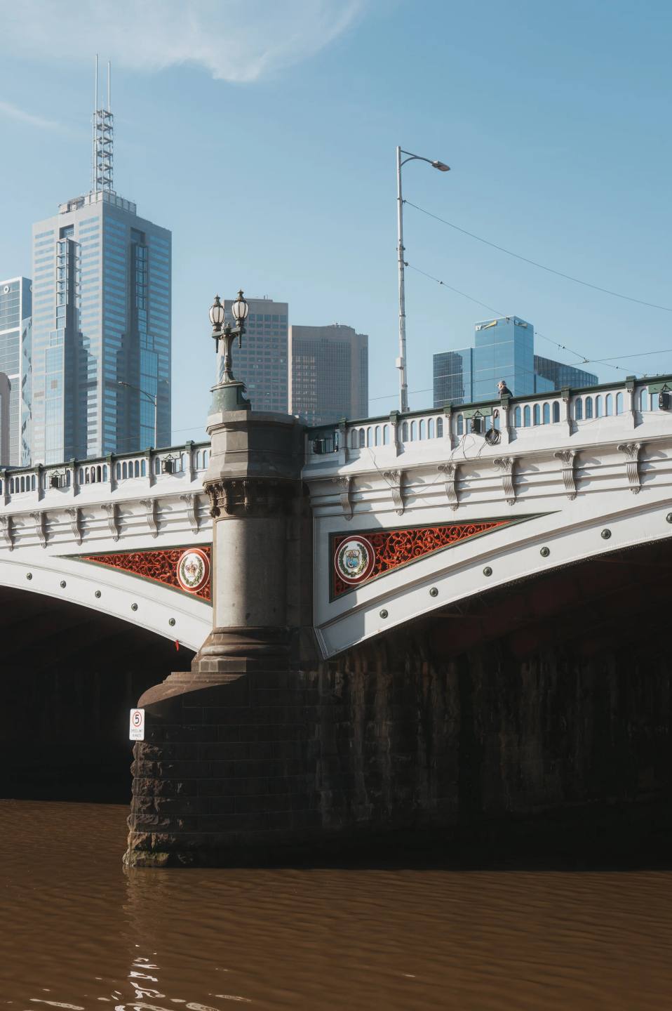A bridge and city buildings beneath a pale blue sky.