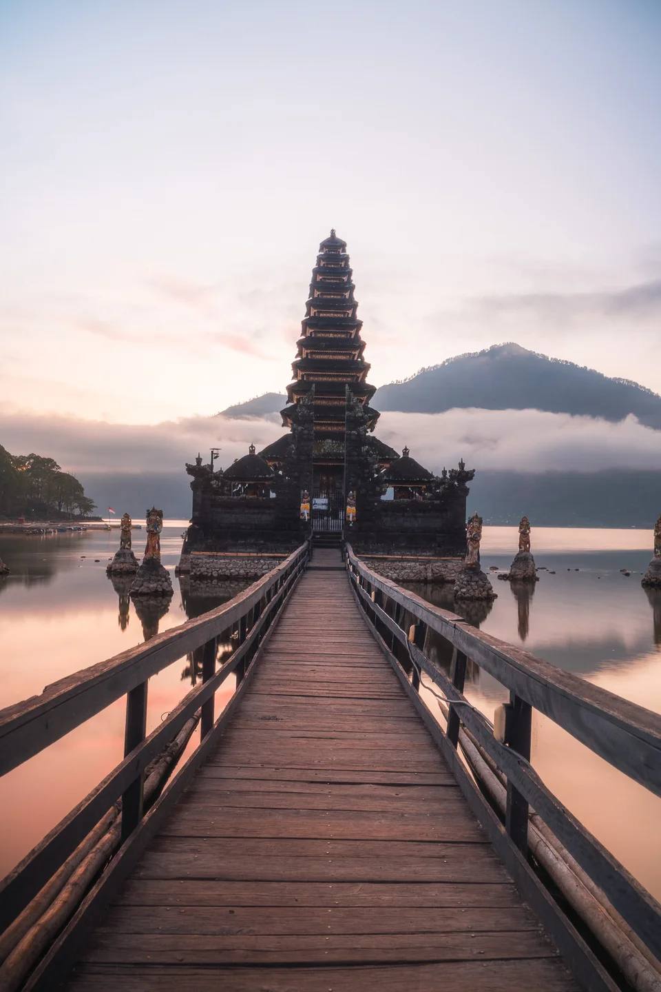 A wooden walkway leading to a lakeside temple at dawn.