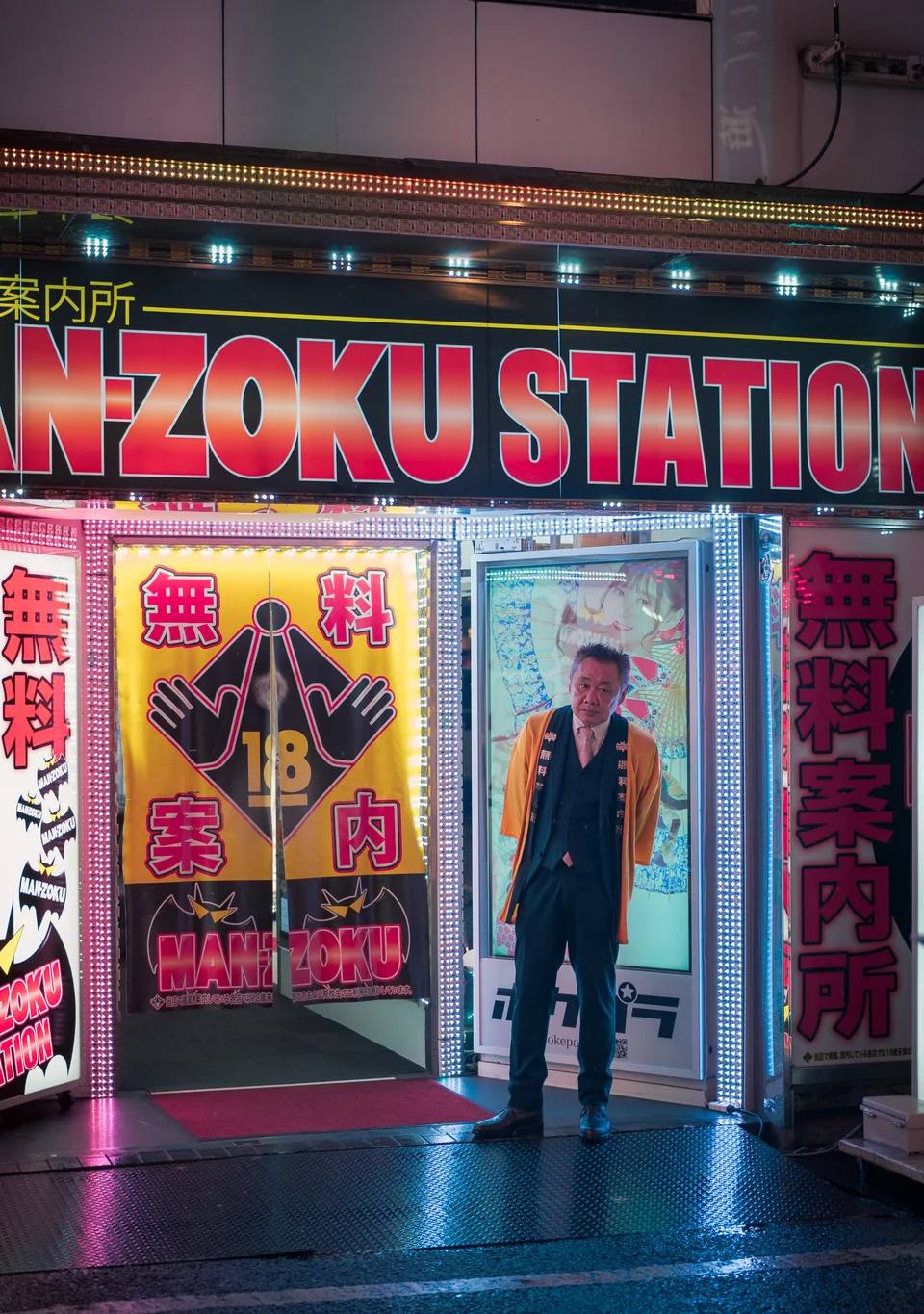A person standing outside a brightly illuminated storefront at night.