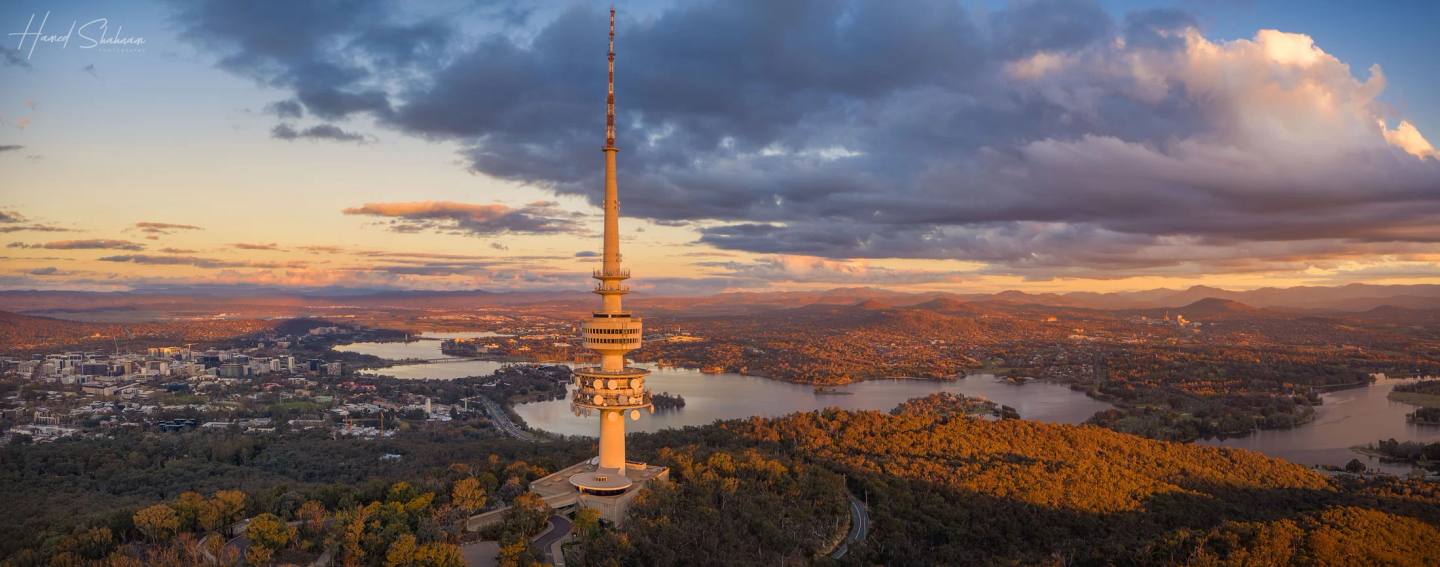 An aerial view of Telstra Tower, wooded hills and Canberra at sunset.