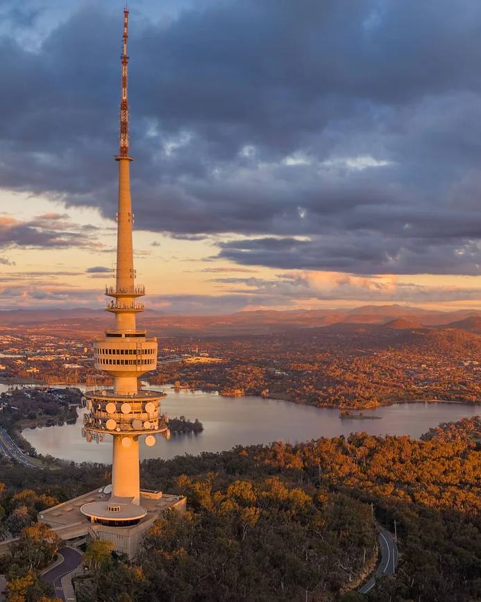 An aerial view of Telstra Tower, wooded hills and Canberra at sunset.