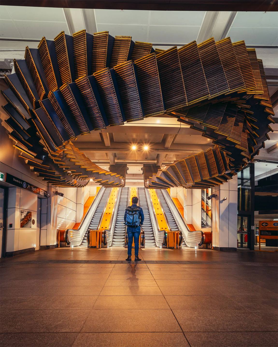 A person approaching escalators beneath a geometric timber ceiling.