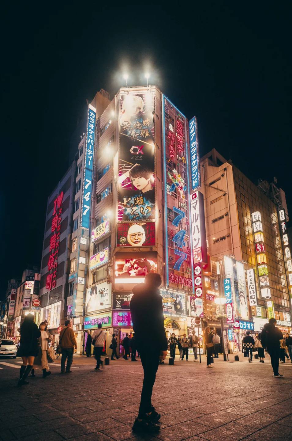Pedestrians beneath illuminated billboards at night.