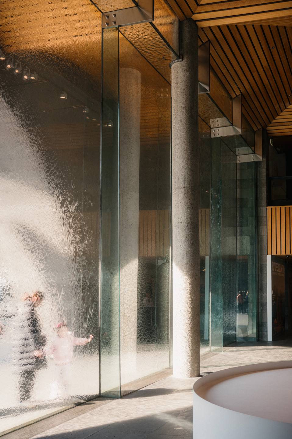 A figure blurred in sunlight through tall gallery windows.