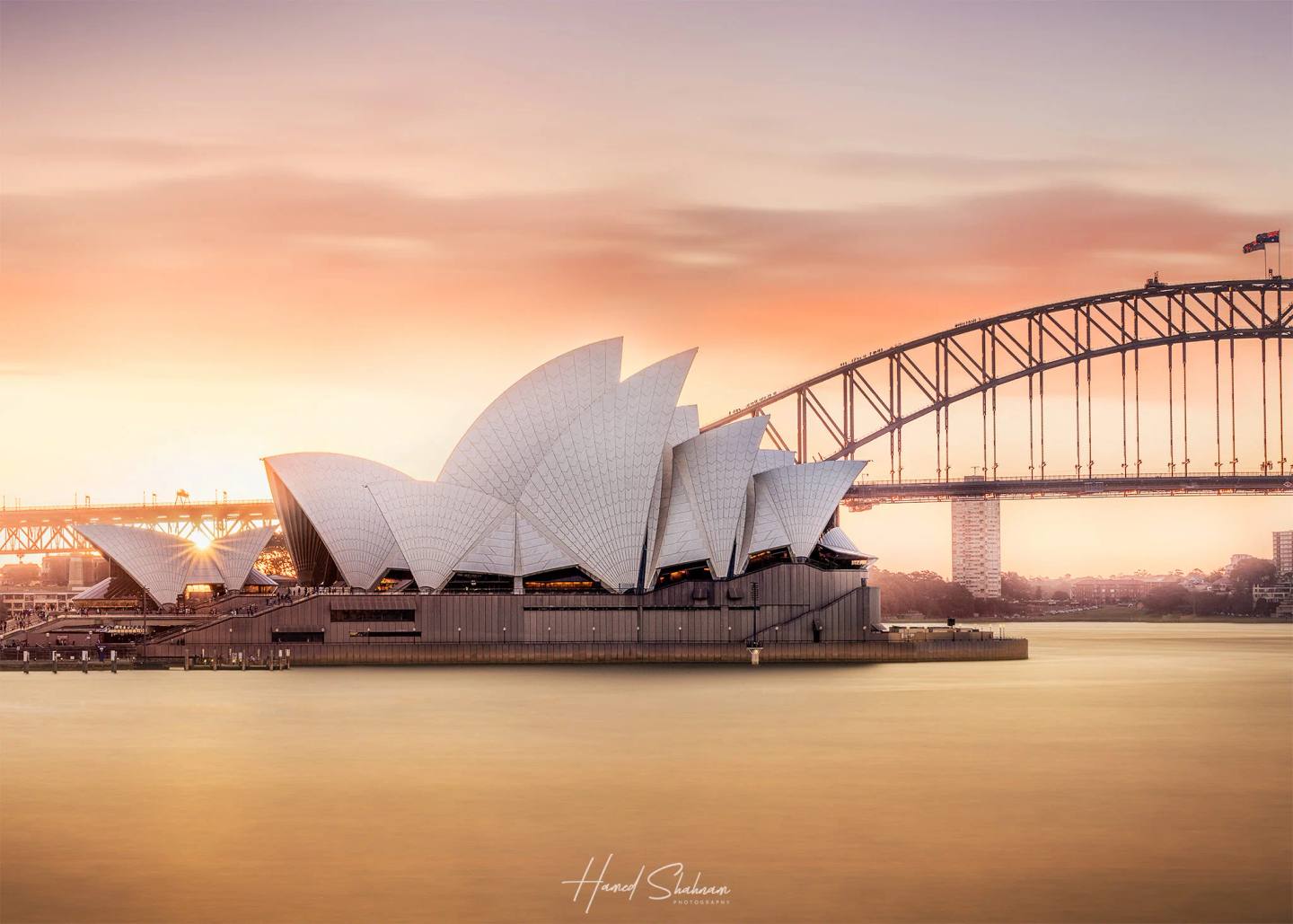 Sydney Opera House and Harbour Bridge reflected in calm water at sunset.