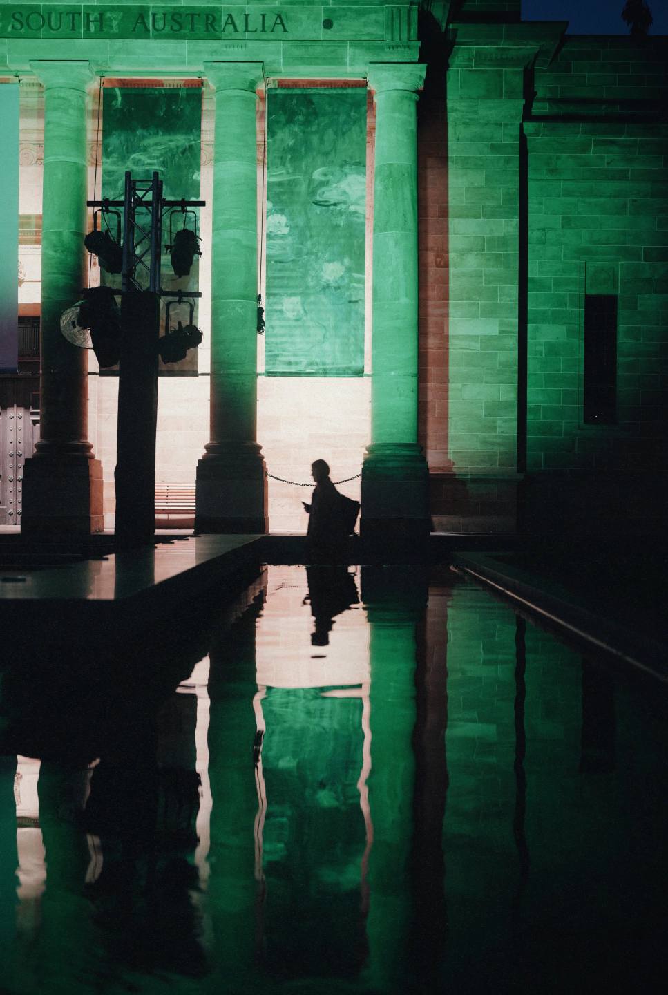 A pedestrian reflected against a green facade.
