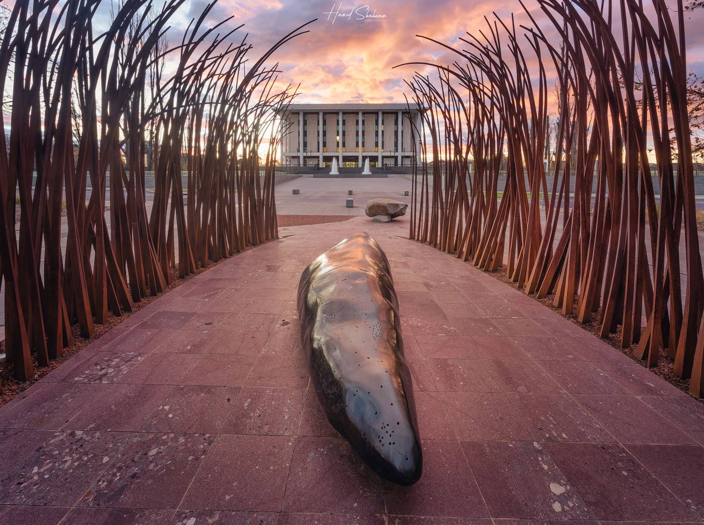 A sculptural passage framing the National Library of Australia at sunset.