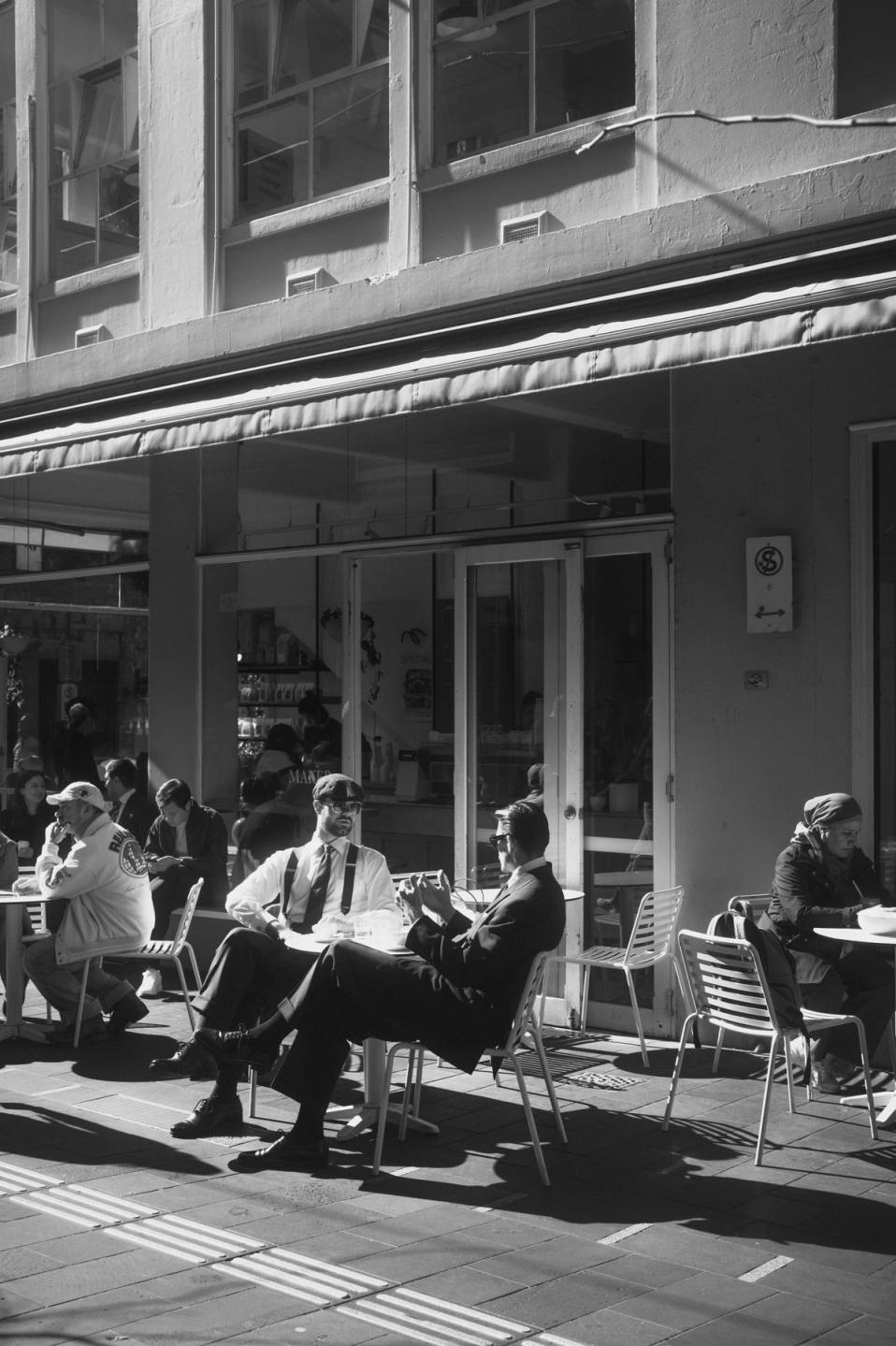 Black and white photo of man setting outside on table and chairs in alleyway