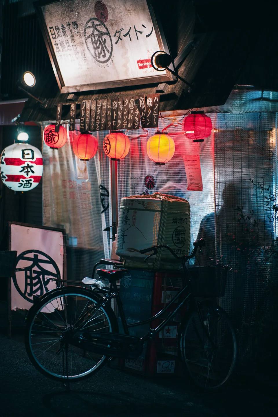 A bicycle outside a small restaurant lit by red lanterns.