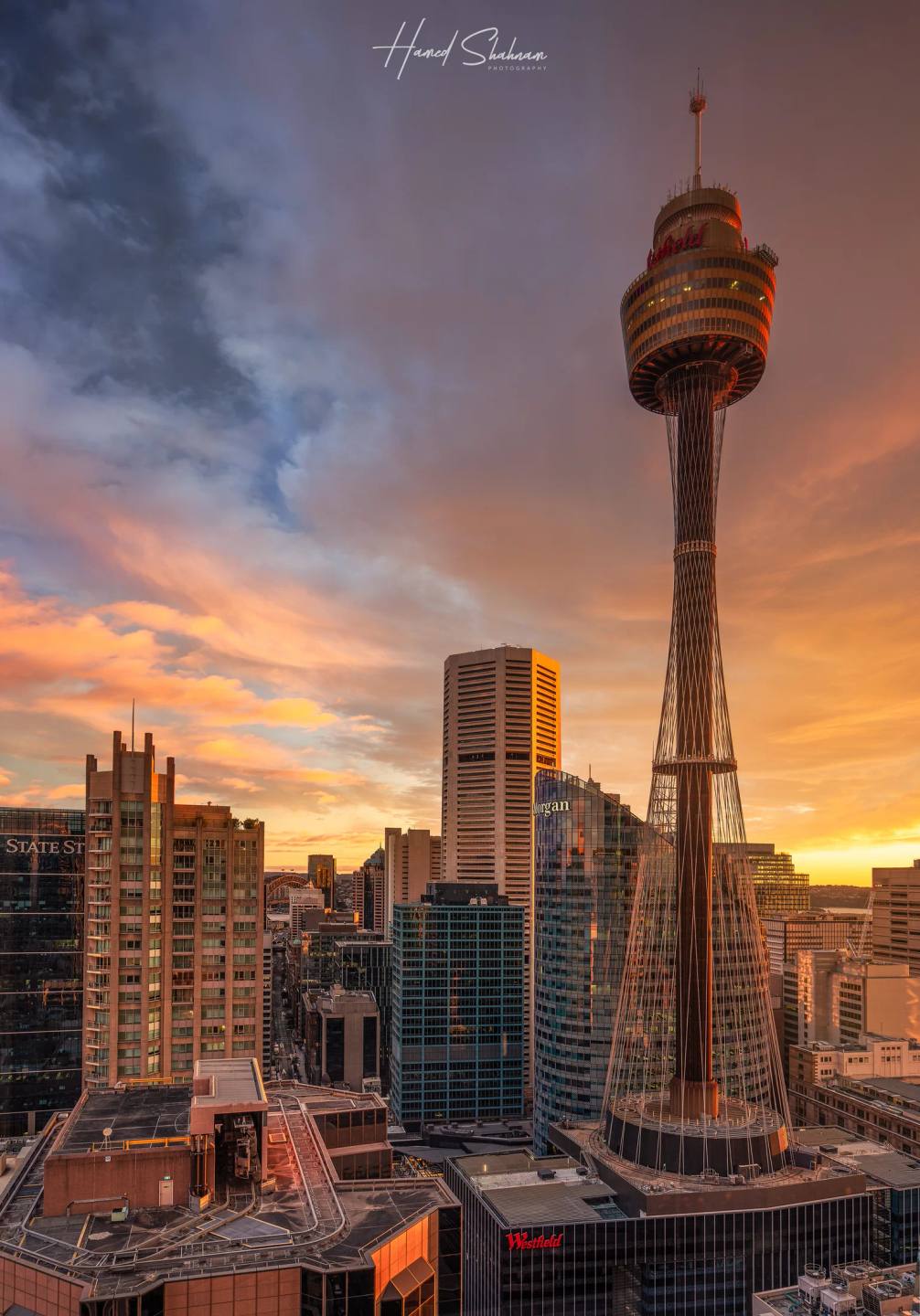 Sydney Tower above city buildings beneath a dramatic sunset sky.