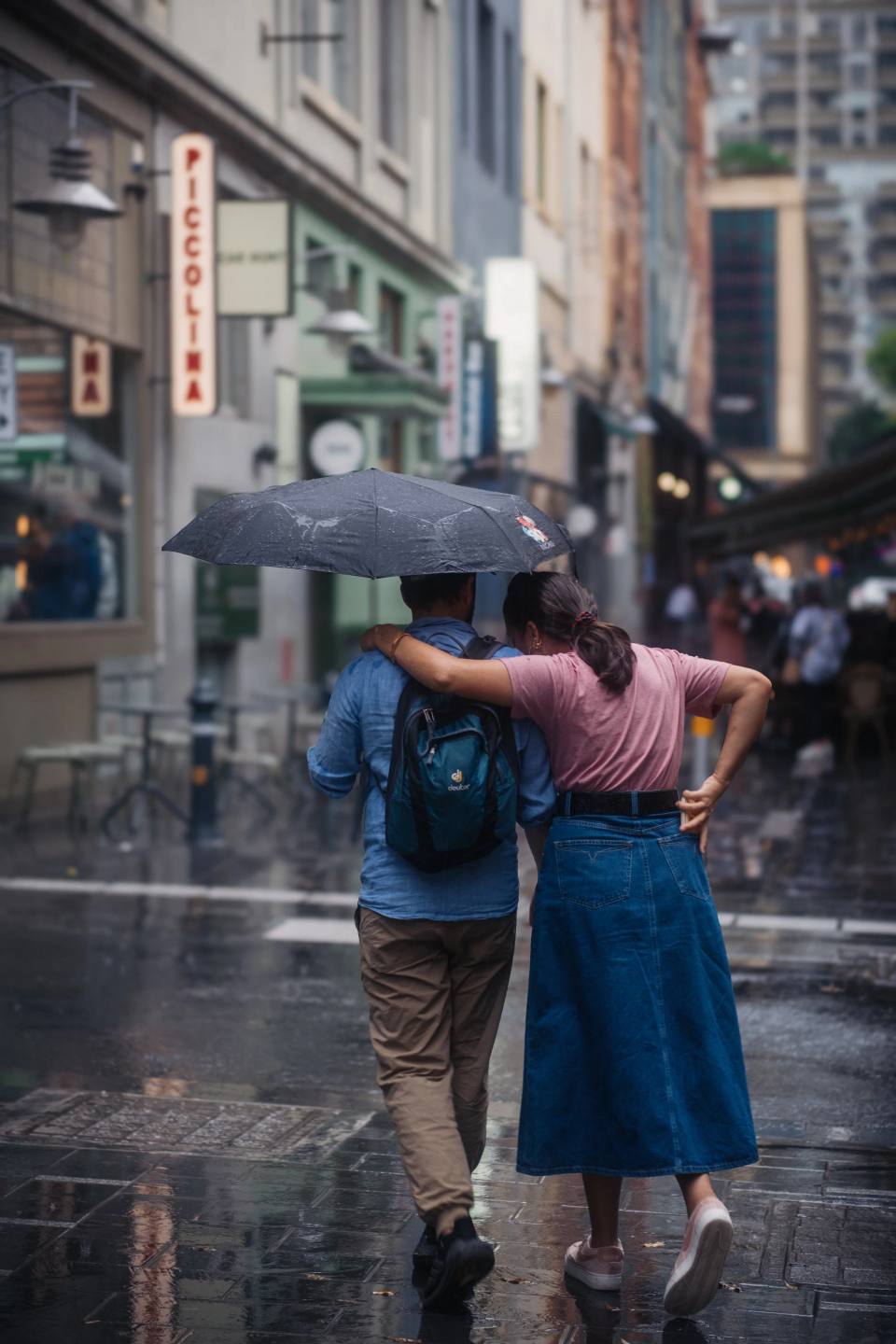Two people sheltering together on a rain-soaked city street.