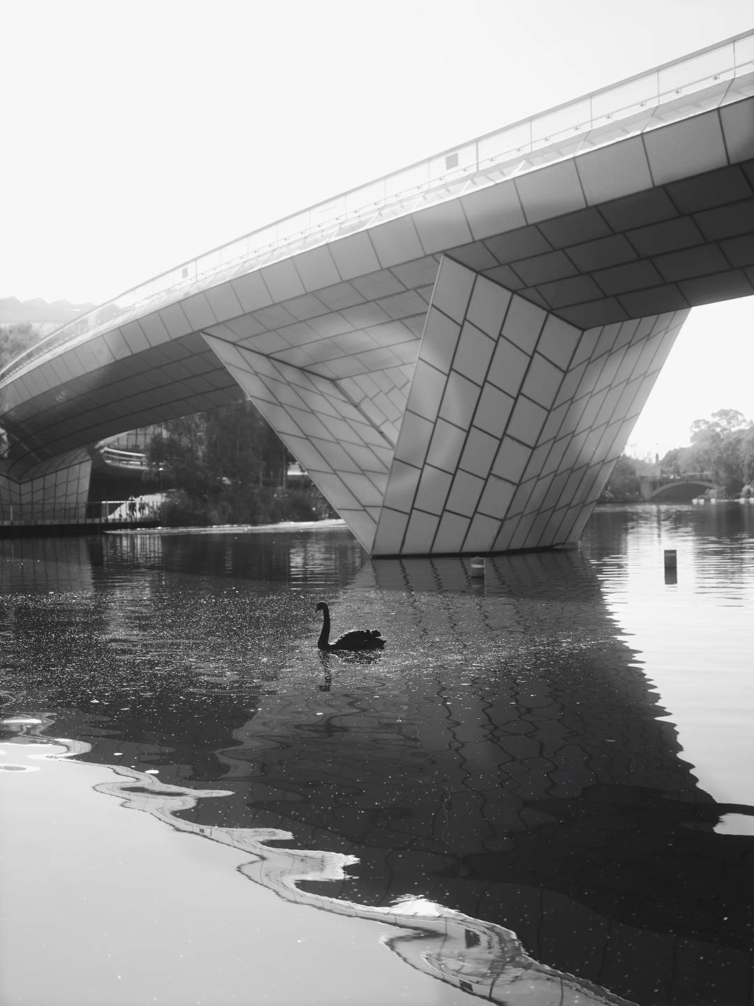An angular bridge reflected in still water, in black and white.
