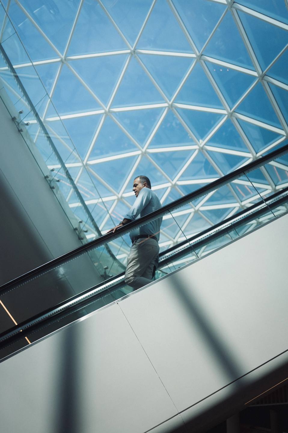 A figure on an escalator beneath a geometric glass roof.