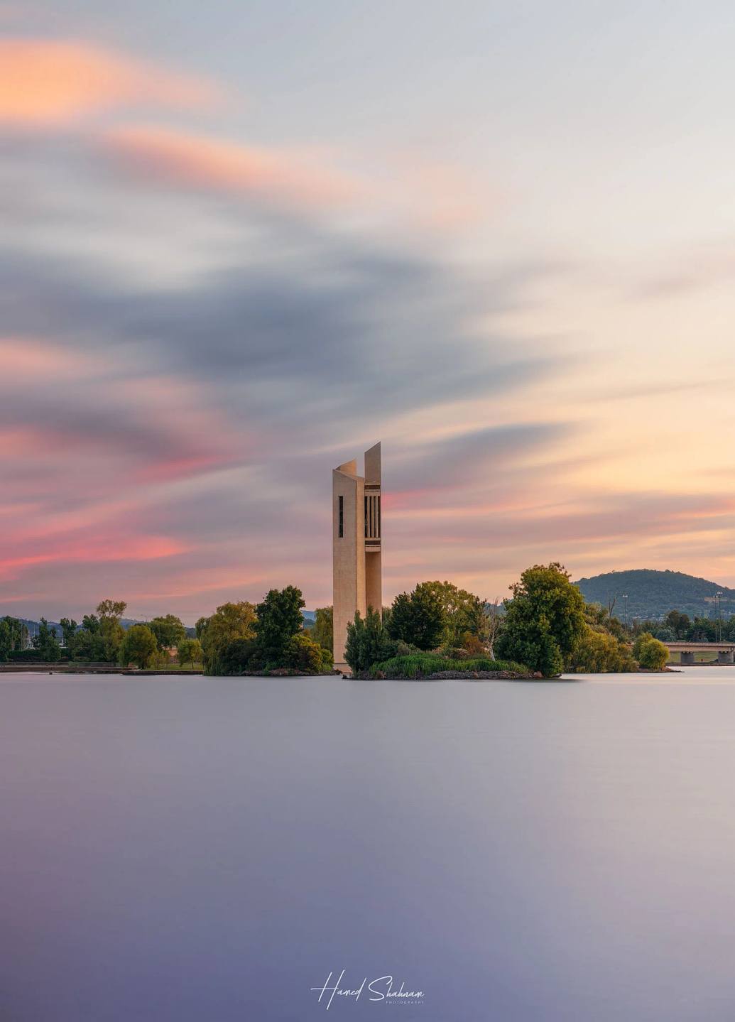 The National Carillon beside still lake water beneath pink evening clouds.