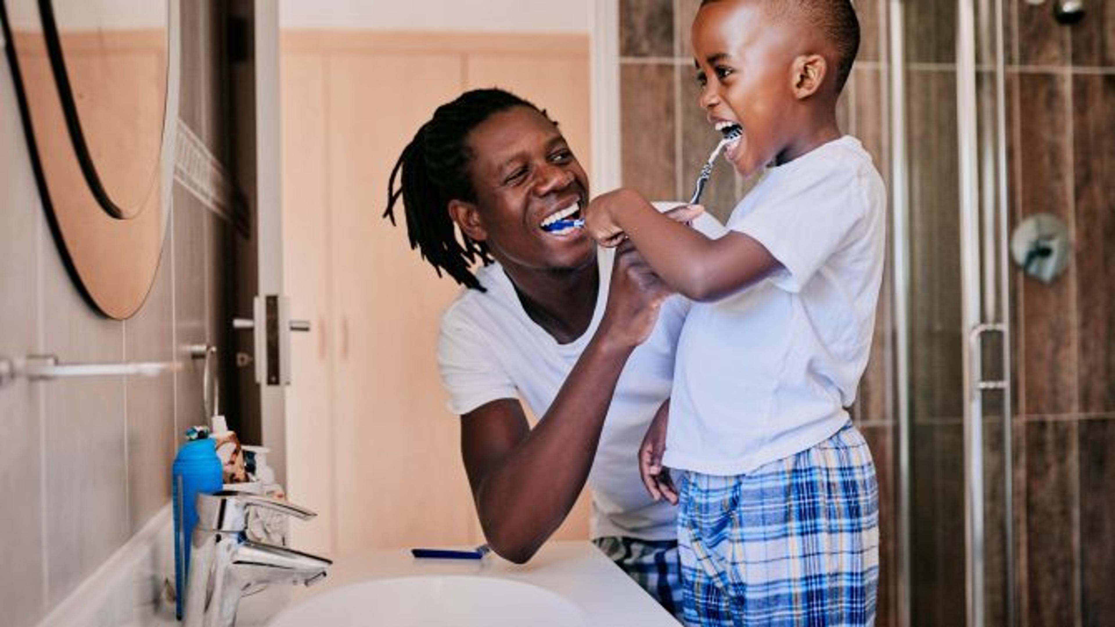 Father helps his son brush his teeth teaching good dental habits to children