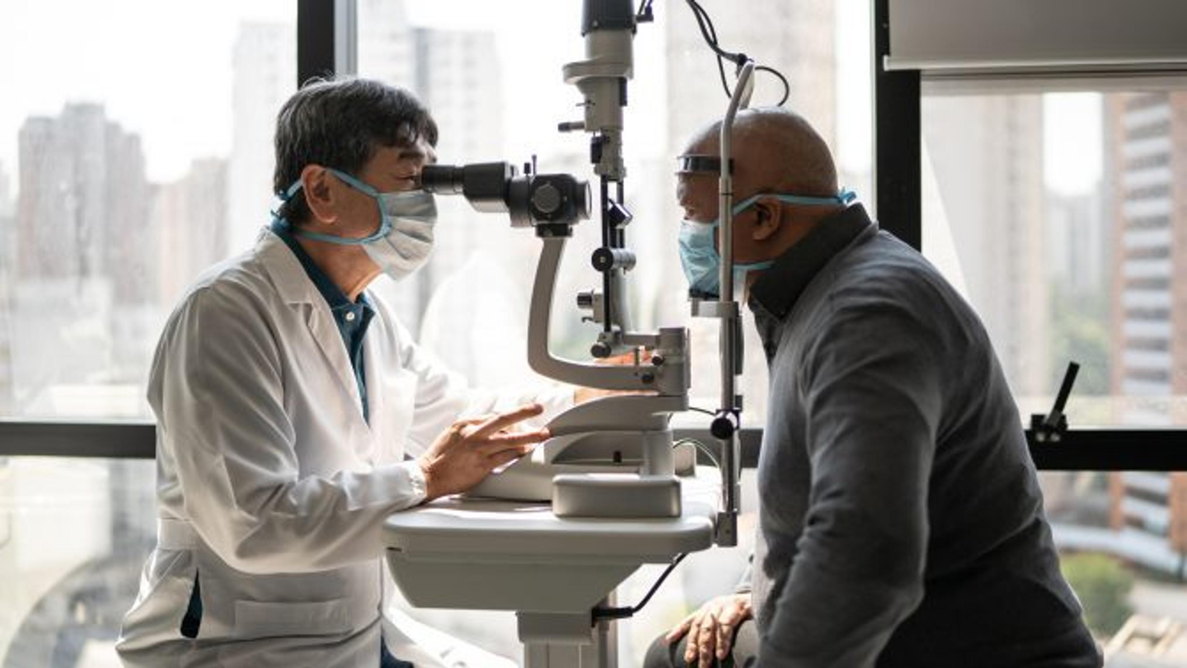 Optometrist examining patient's eyes - wearing face mask