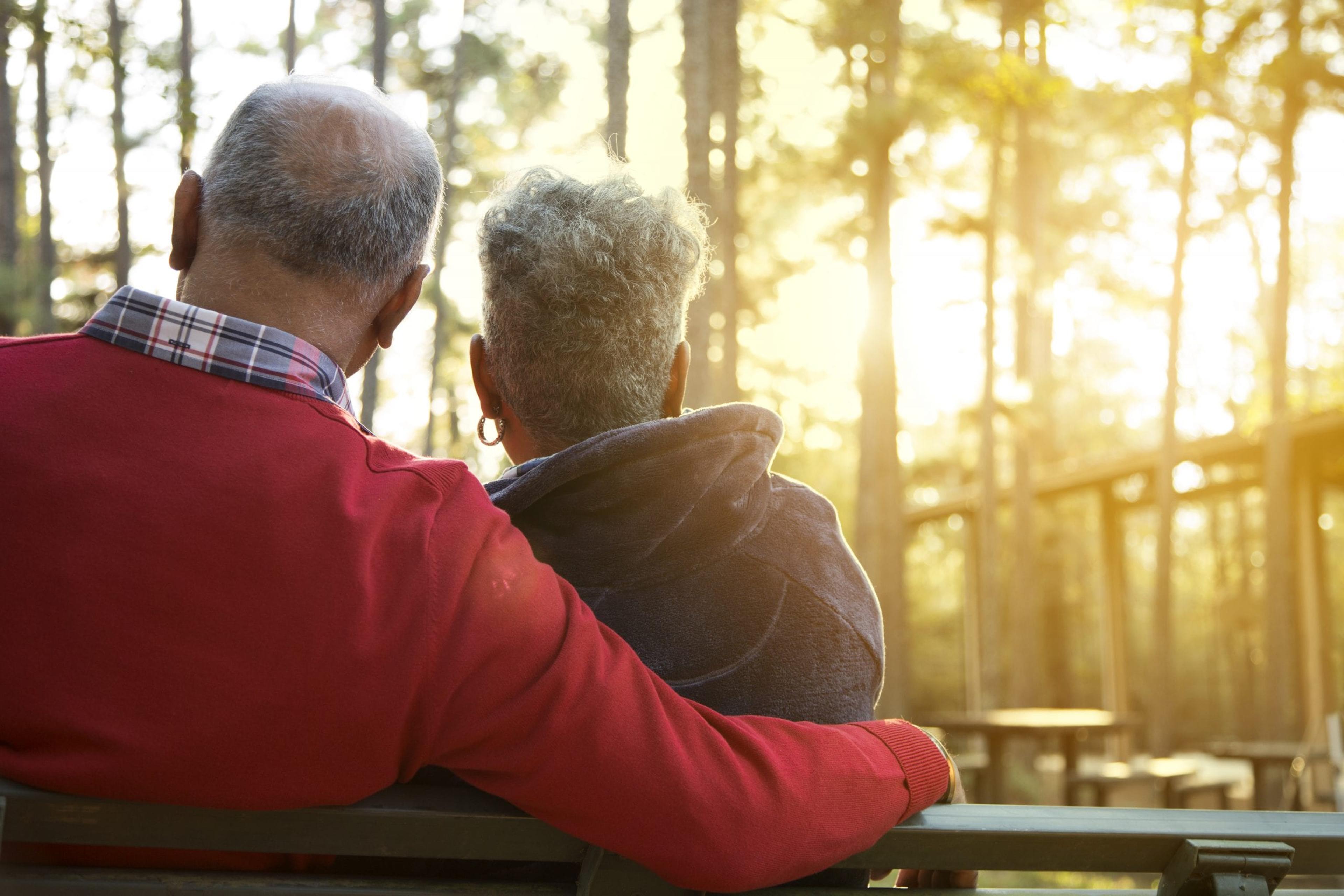 Older couple sitting on a bench watching the sunset.