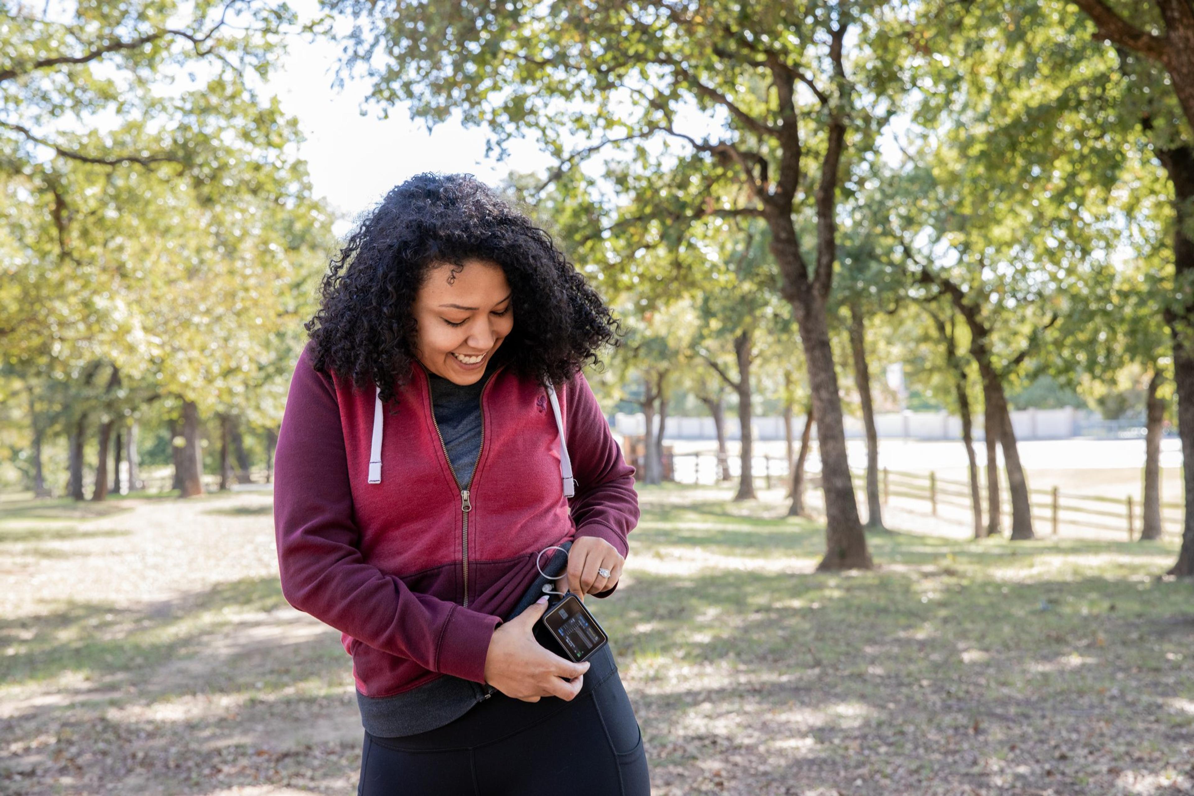 Young woman with diabetes checks insulin pump and blood sugar monitor while hiking outdoors