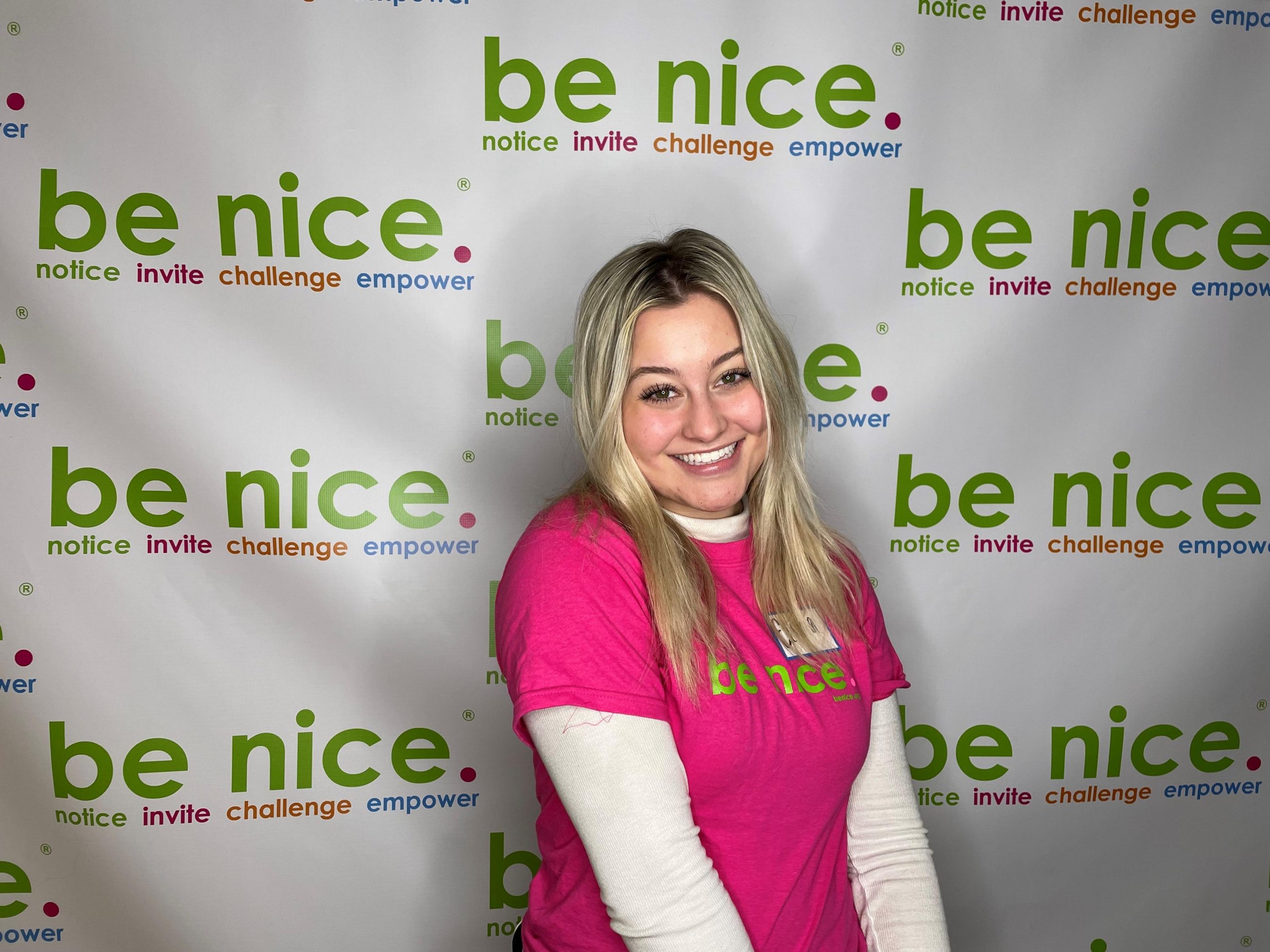 A high school student poses in front of a step and repeat at the be nice. student symposium for mental health