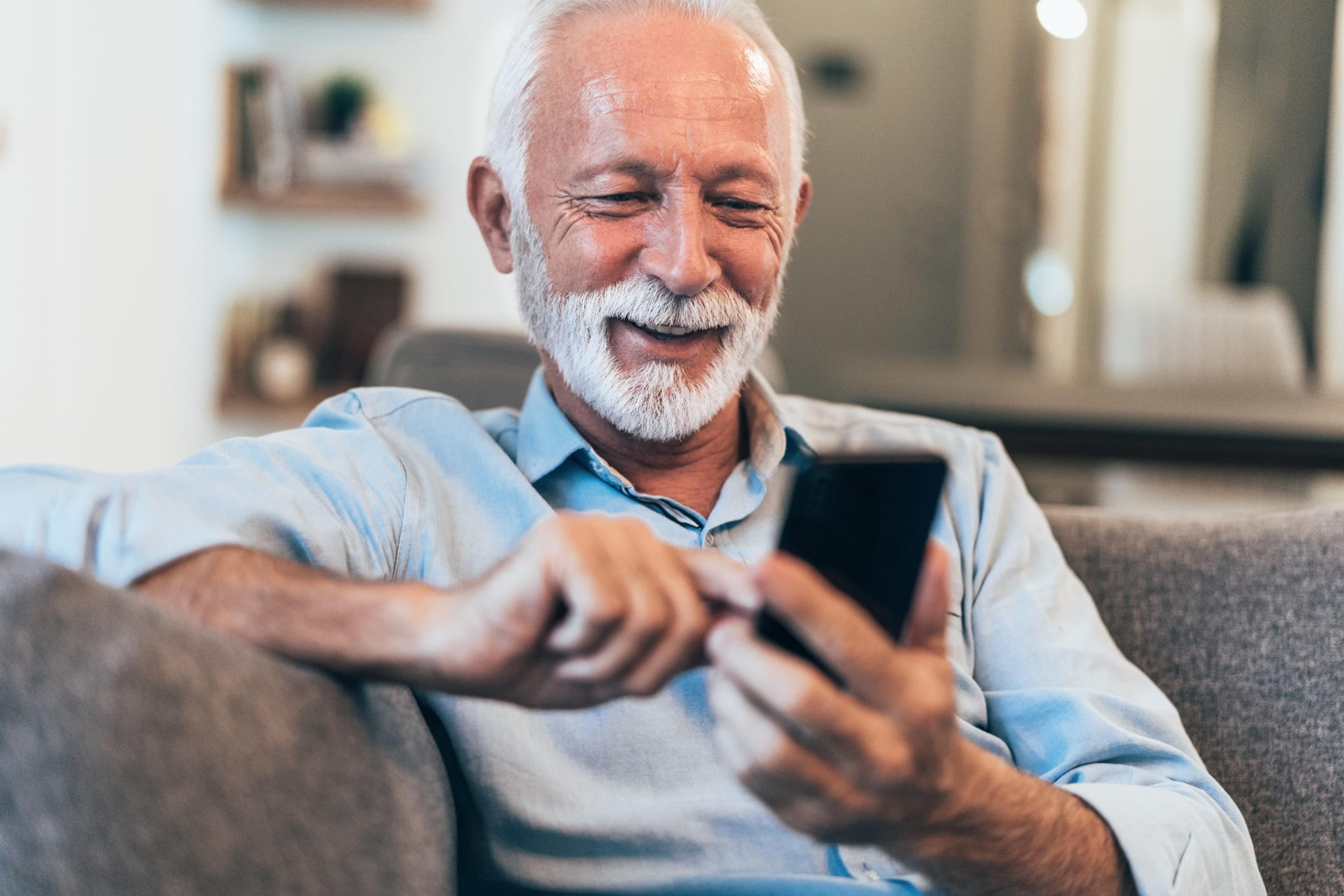Grey-haired man uses his cell phone while sitting on the couch