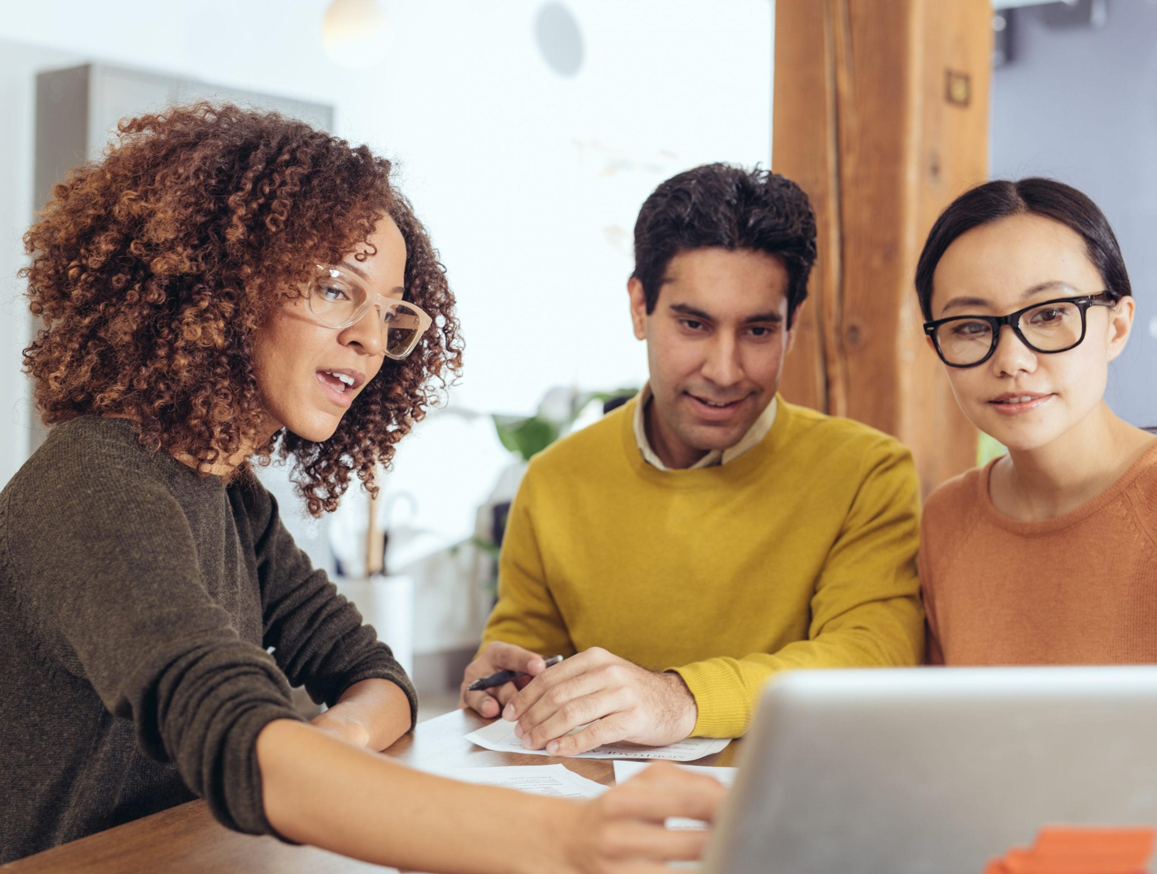 Image of three diverse workers looking at a laptop.