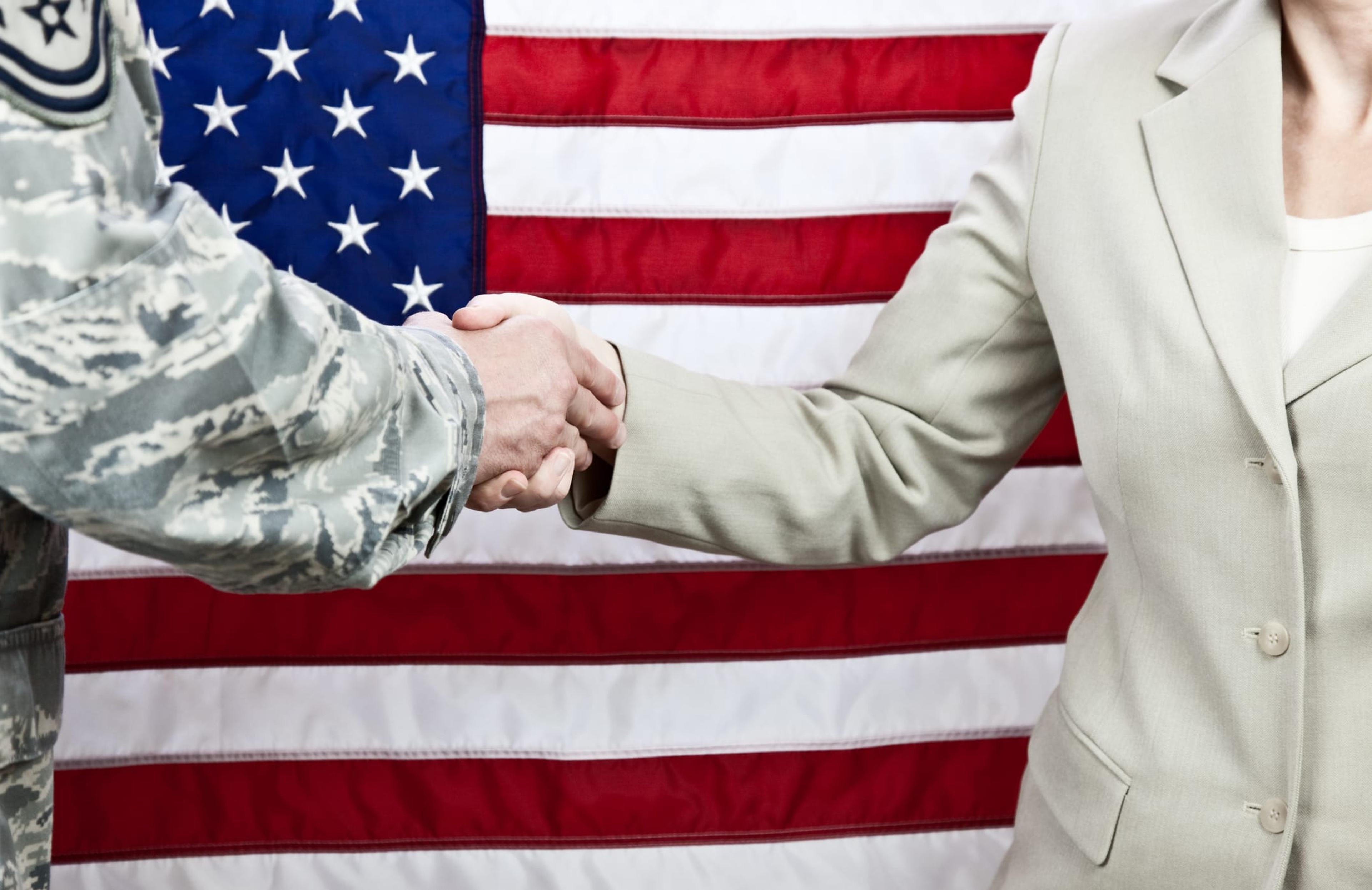 Military member shaking hands with a cilivian with an American flag in the background