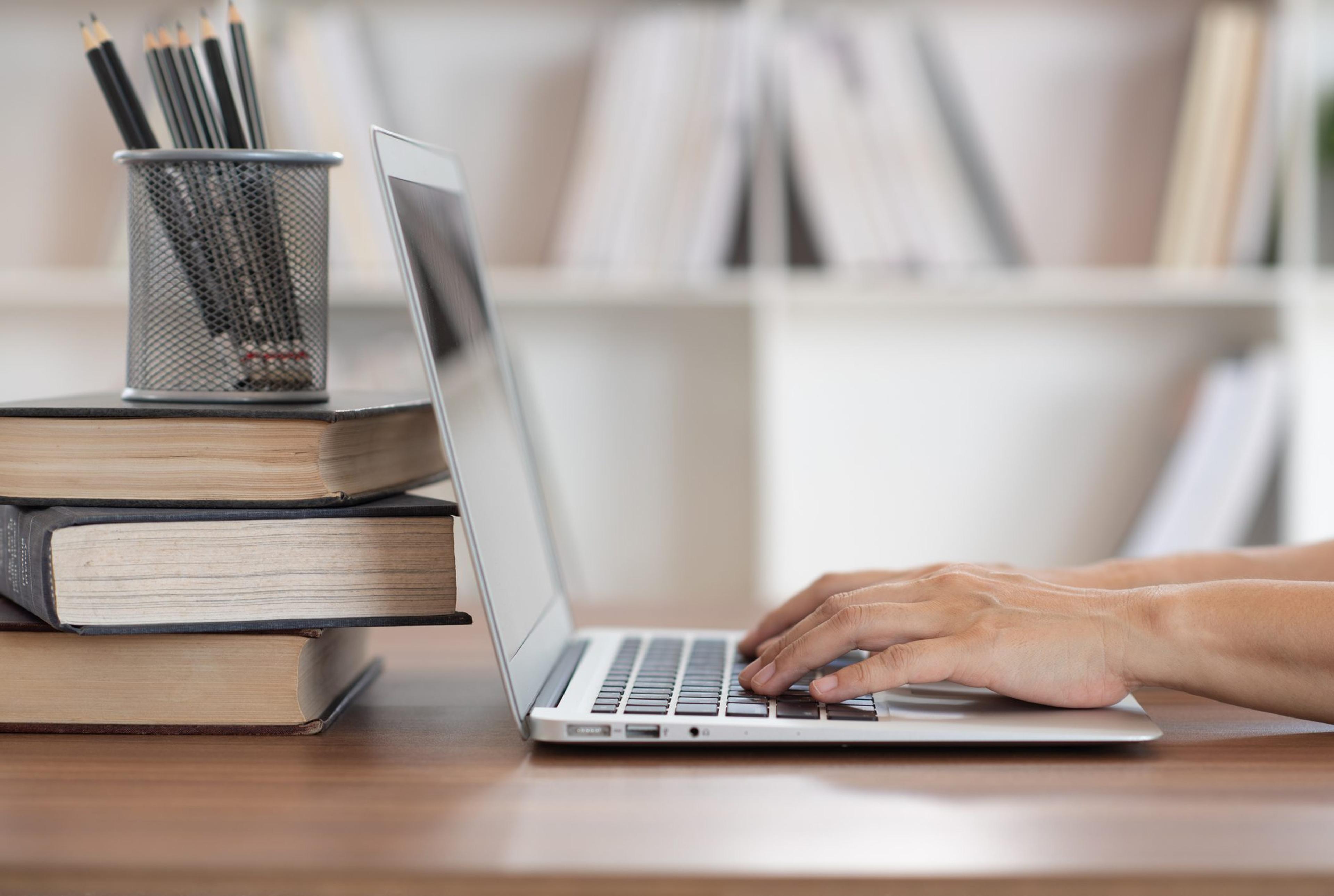 Woman using laptop computer with book stack on desk in library. e-book digital technology and e-learning class concept.