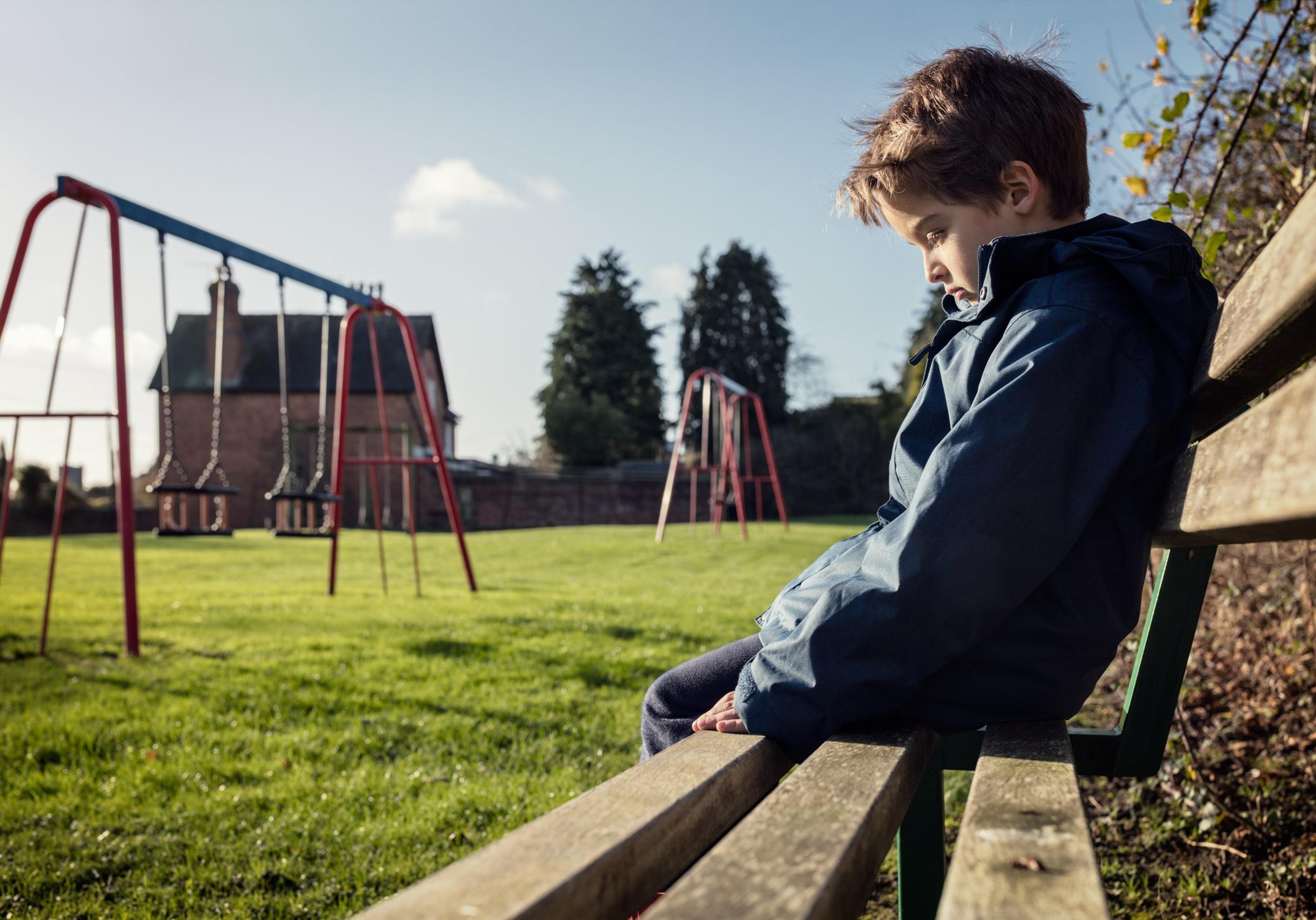 Lonely child sitting on play park playground bench