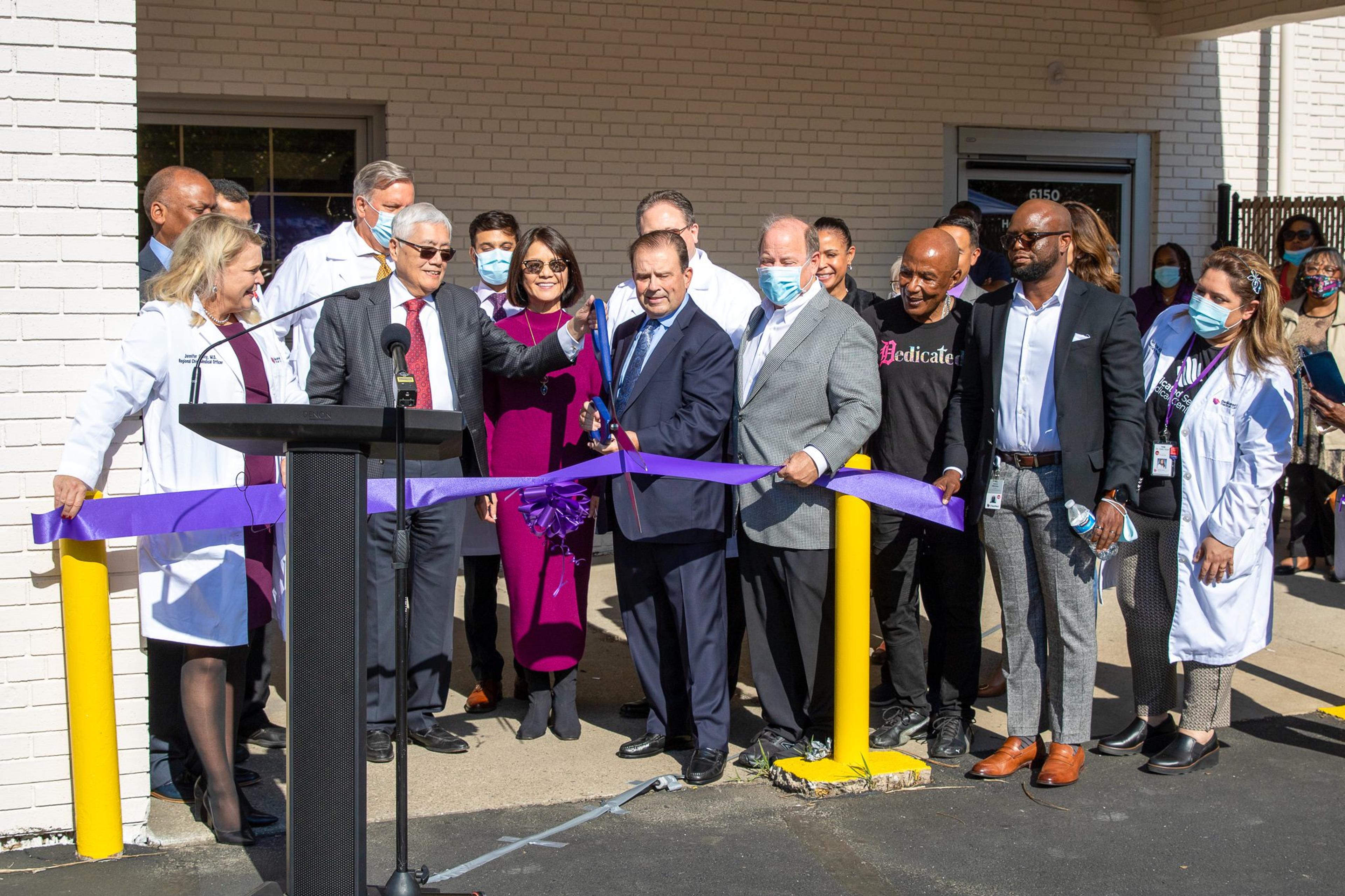 A group of people gather for a ribbon cutting in front of a doctor's office