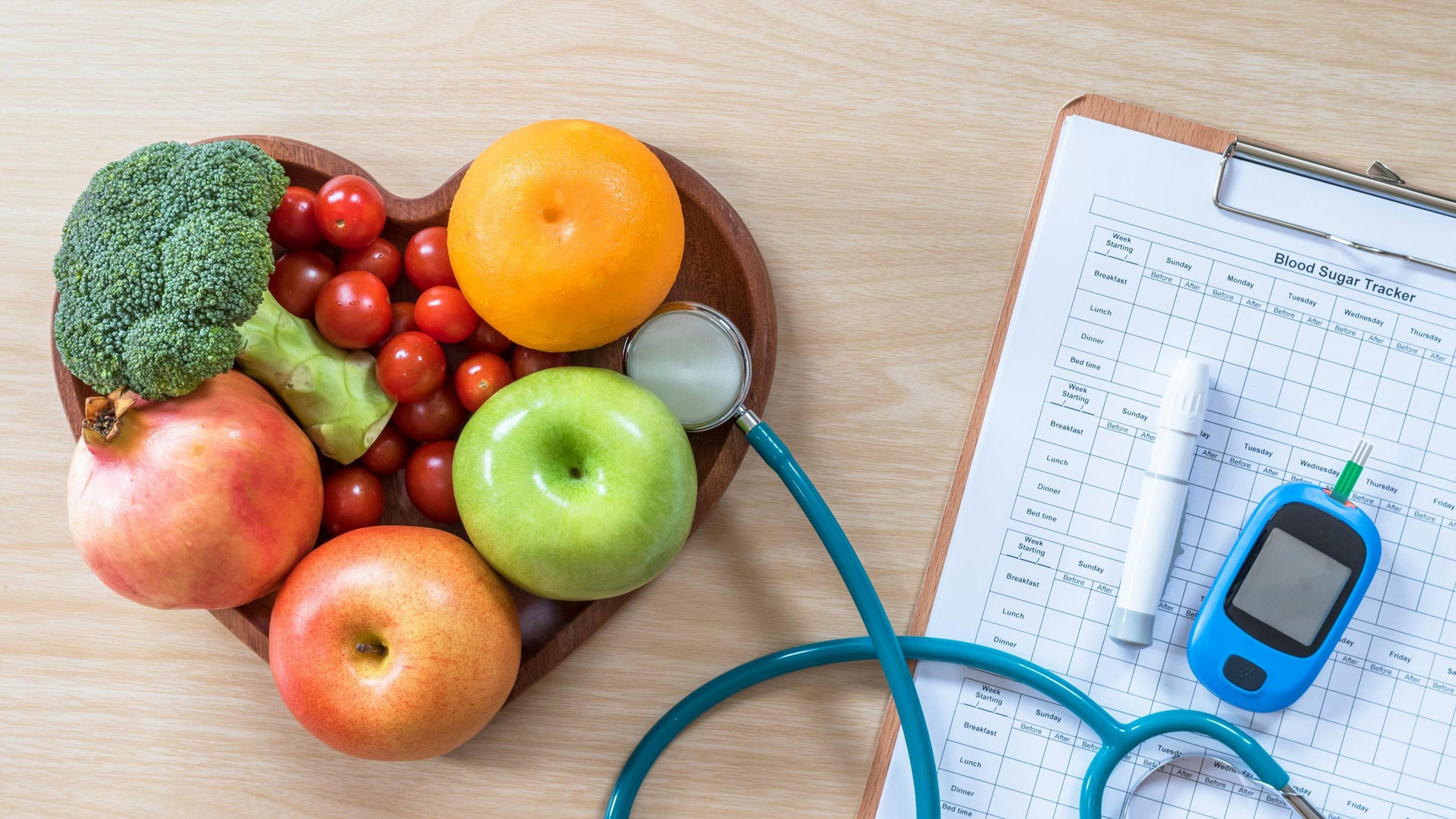 Bowl of fruit and vegetables with stethoscope and diabetes monitor