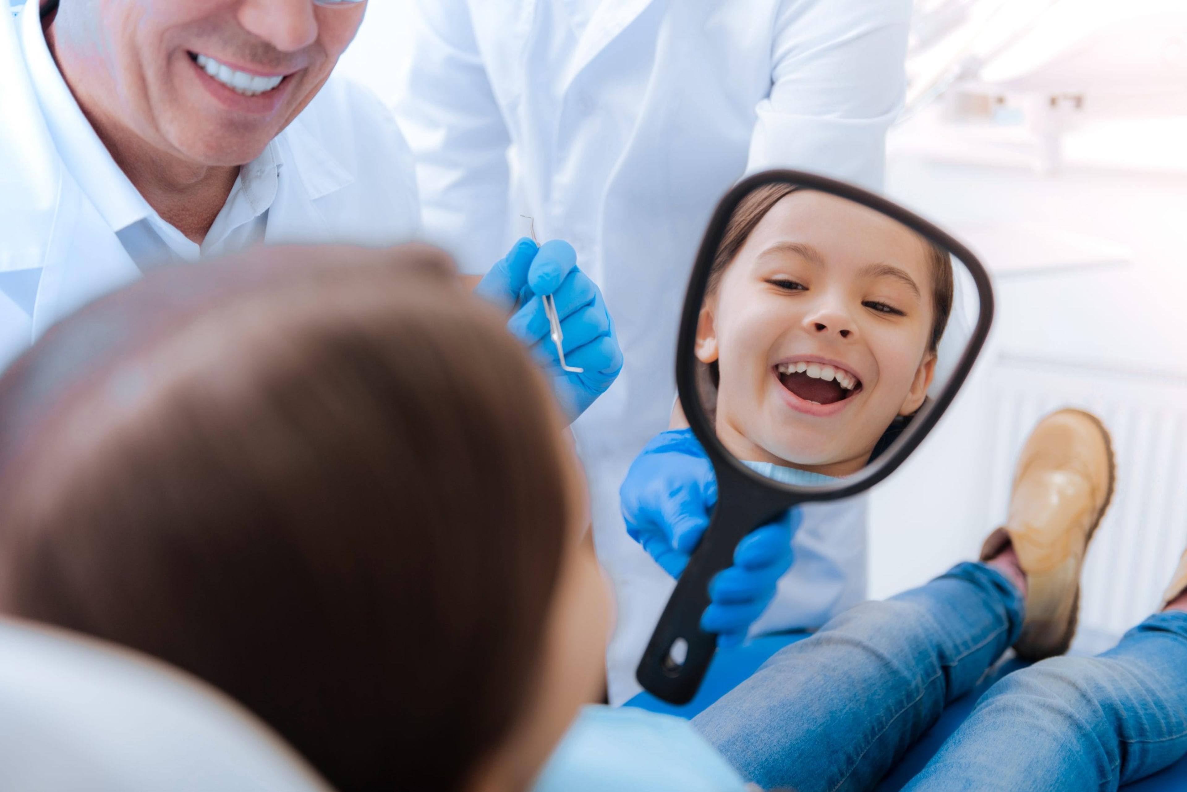 Girl looking at her smile in the mirror at dentist's office.