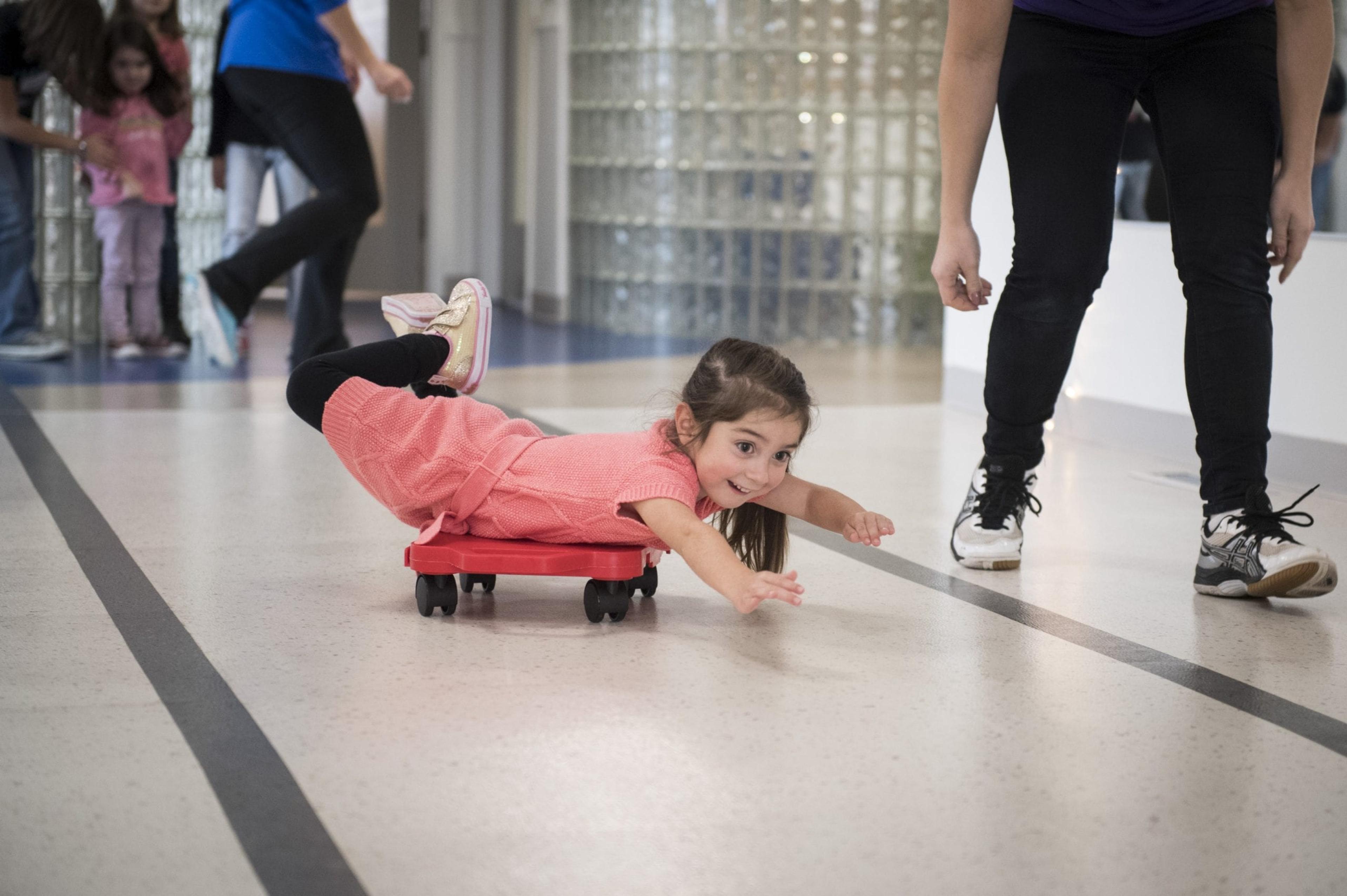 A child visiting the Children's Healing Center rides a scooter across the floor on her belly.