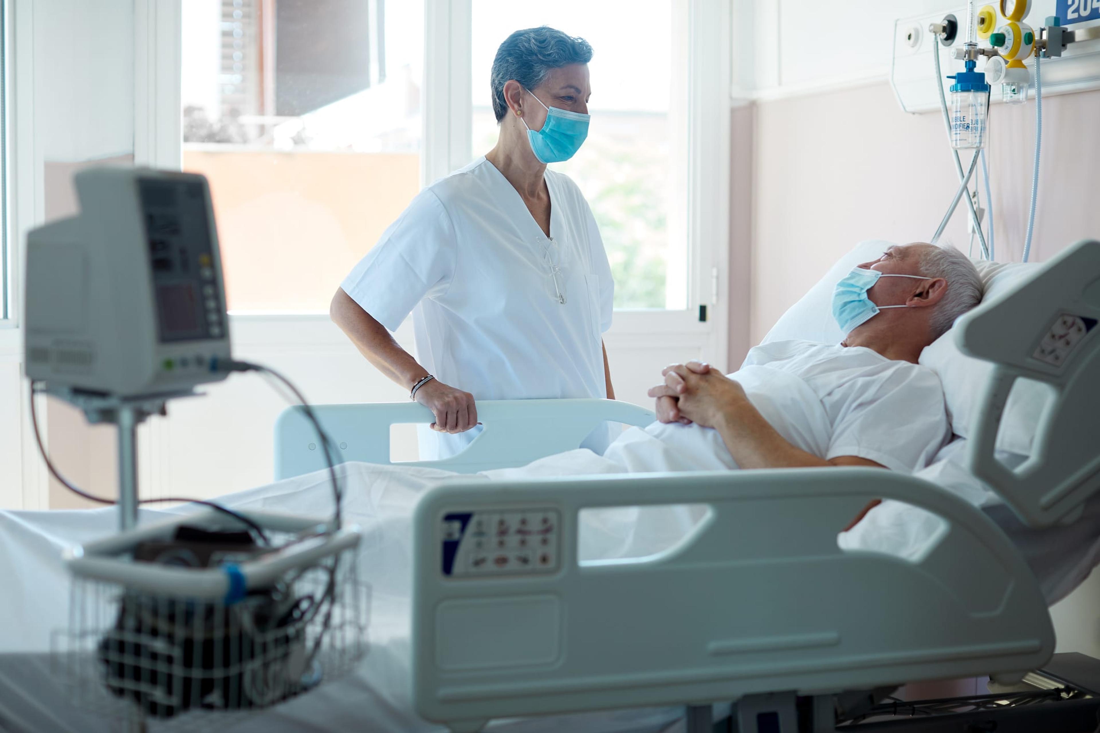 Doctor wearing a mask consulting with a patient in a hospital bed