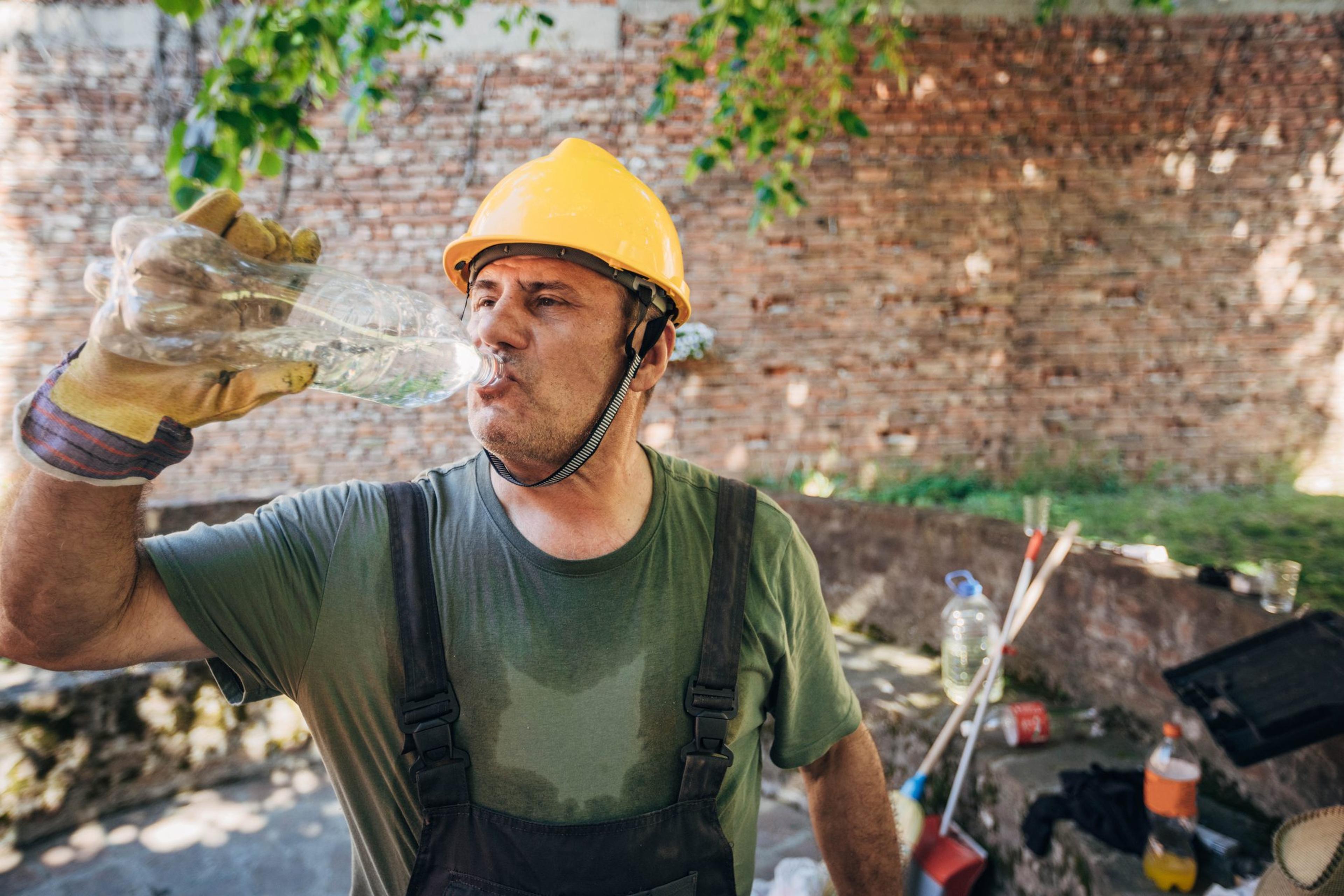 A middle aged construction worker sweating outside with high blood pressure takes a drink of water to cool down in the summer heat and humidity