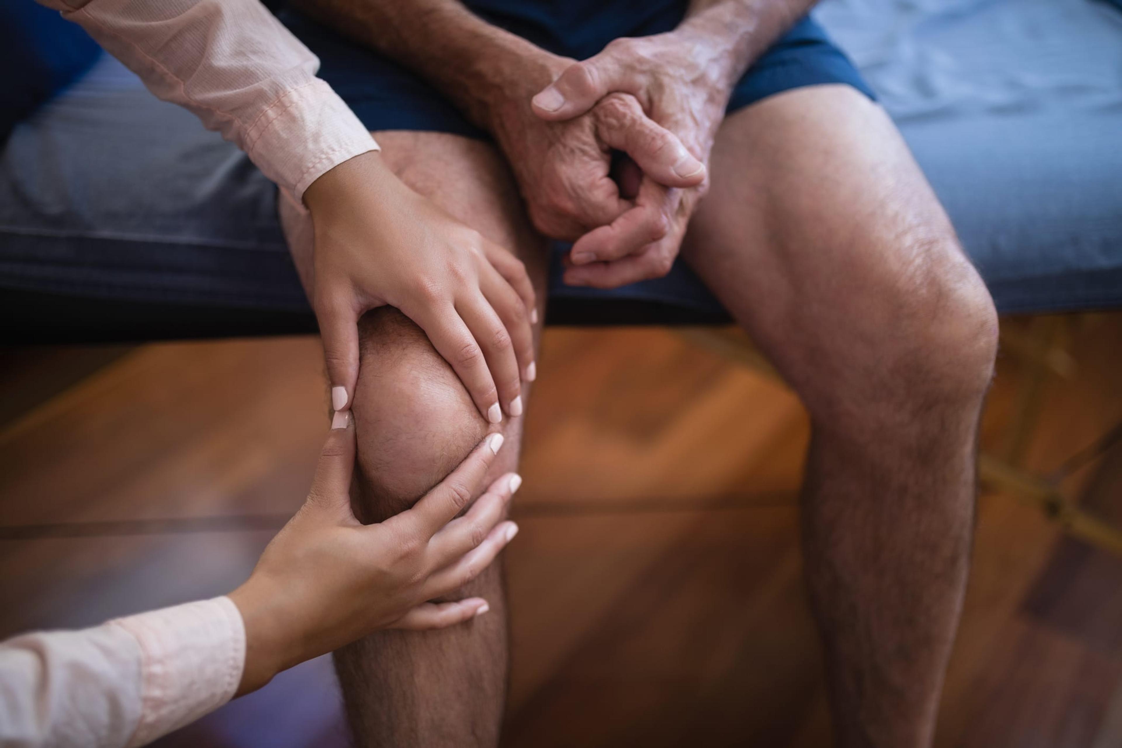 high angle view of physical therapist examining knee while senior male patient sitting on bed