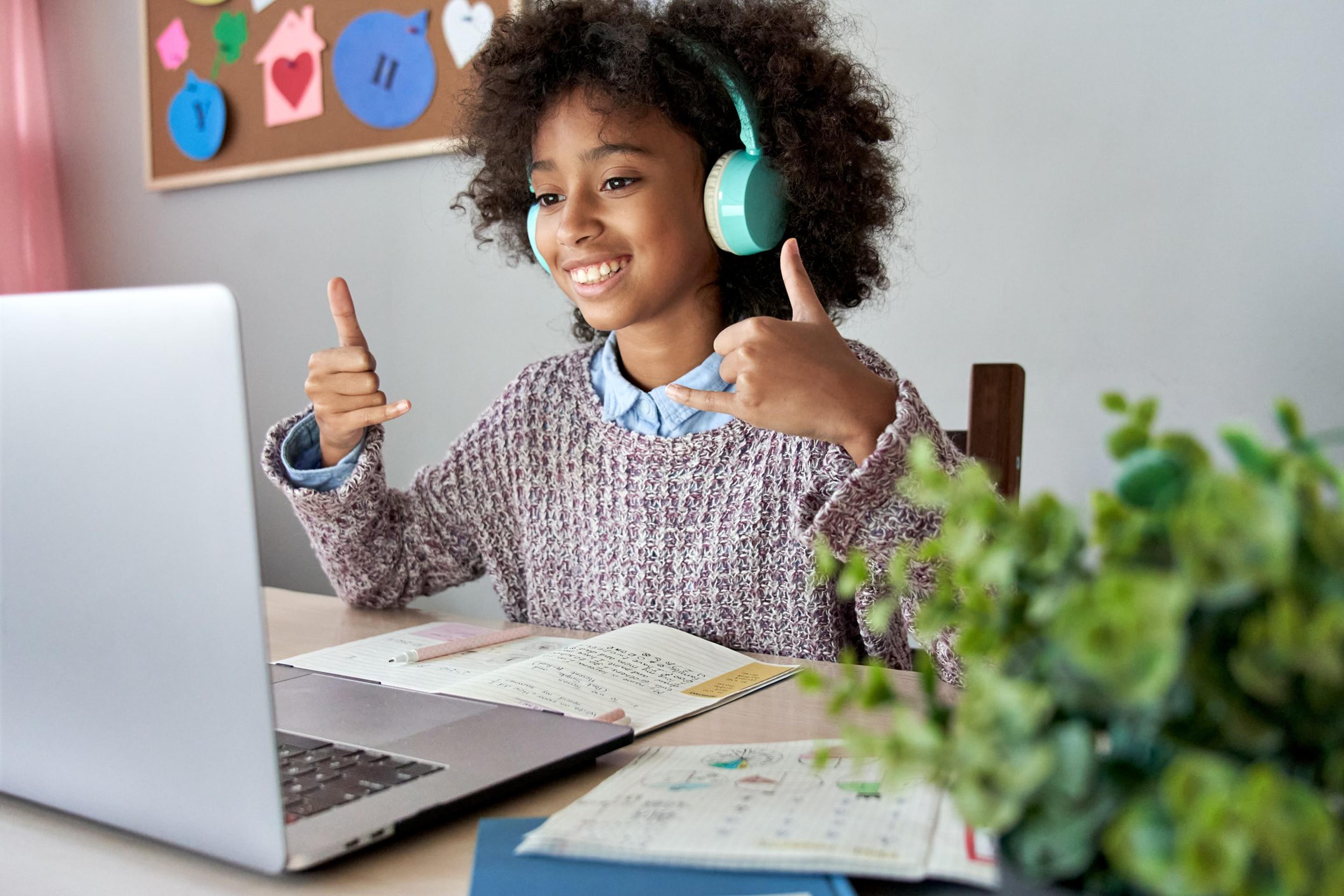Smiling girl with headphones gives thumbs up while doing a virtual learning session