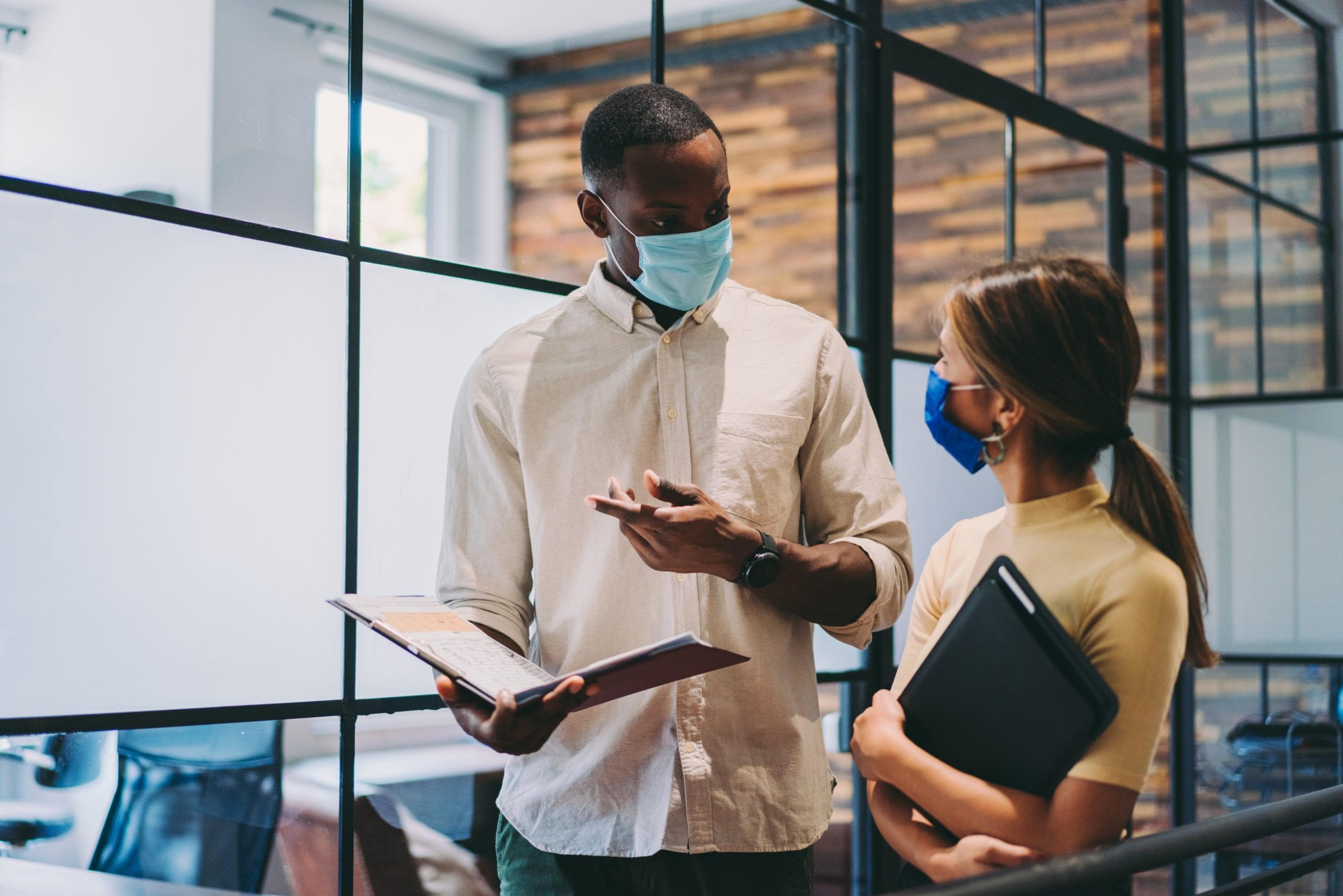 Co-workers discussing work wearing masks