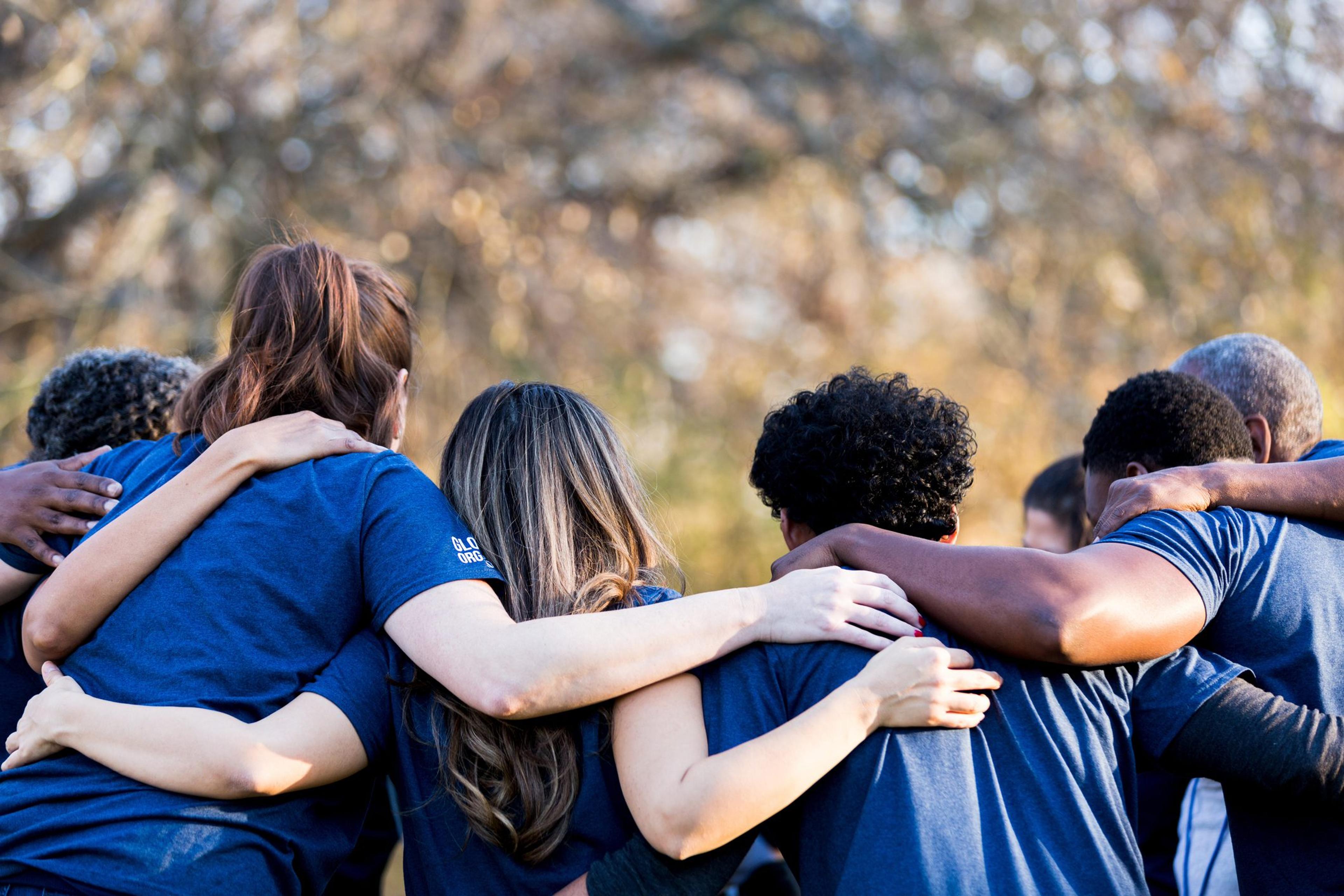 A diverse group of people link arms over peers' backs.