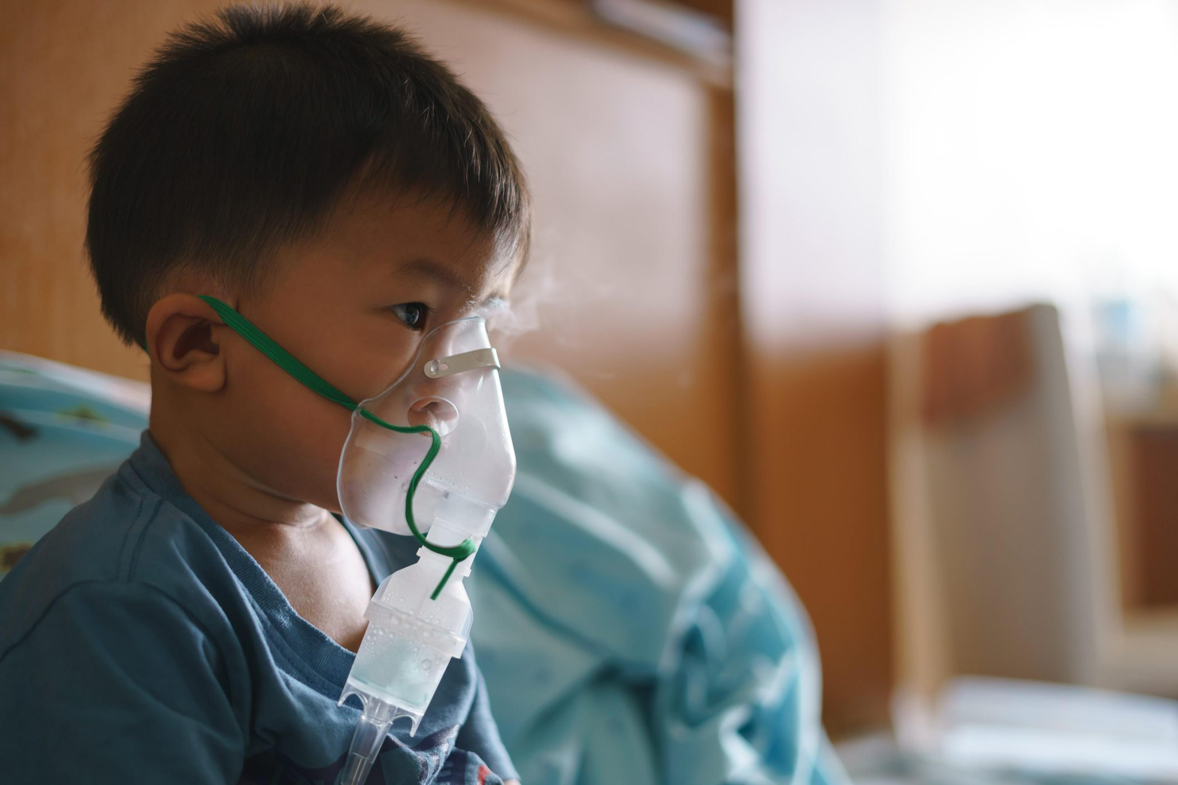 Asian boy using inhaler containing medicine to stop coughing