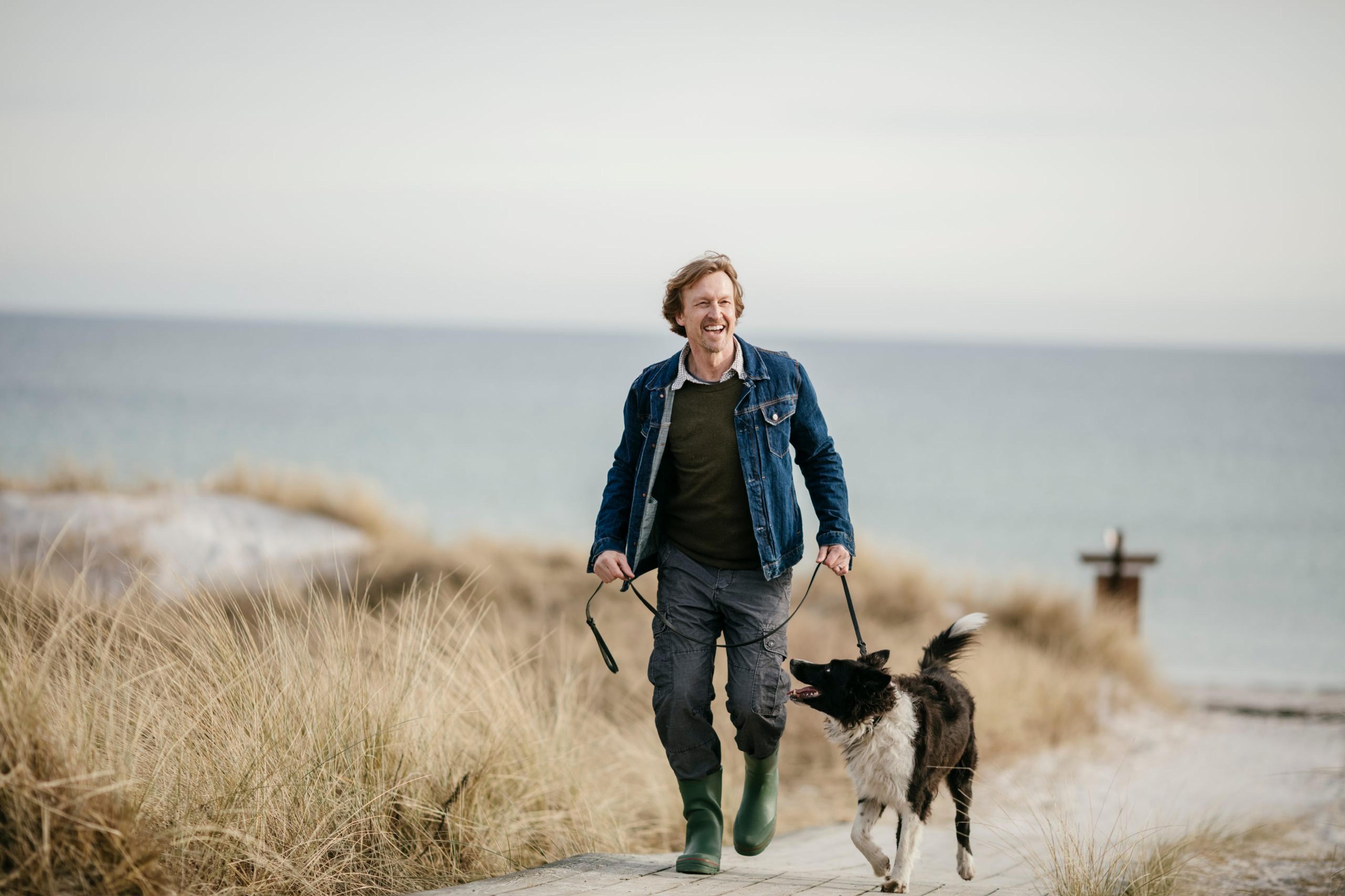 Photo of a man walking by the beach with his dog