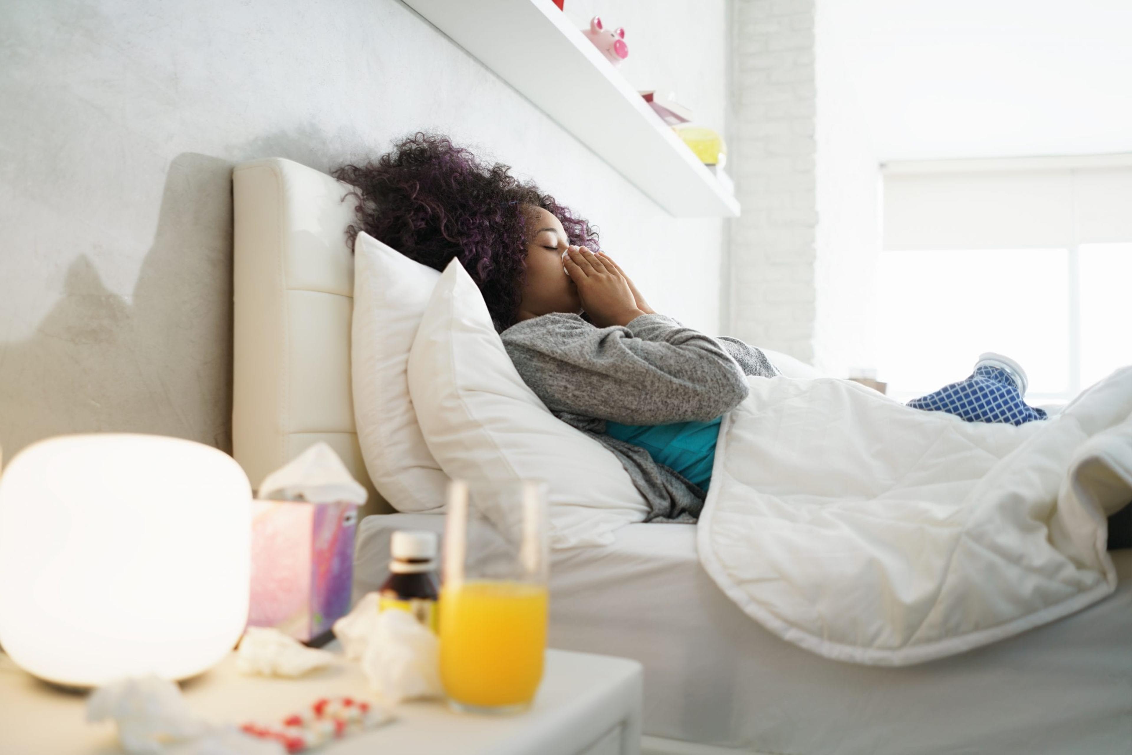 Sick girl at home with medication and orange juice at her bedside.