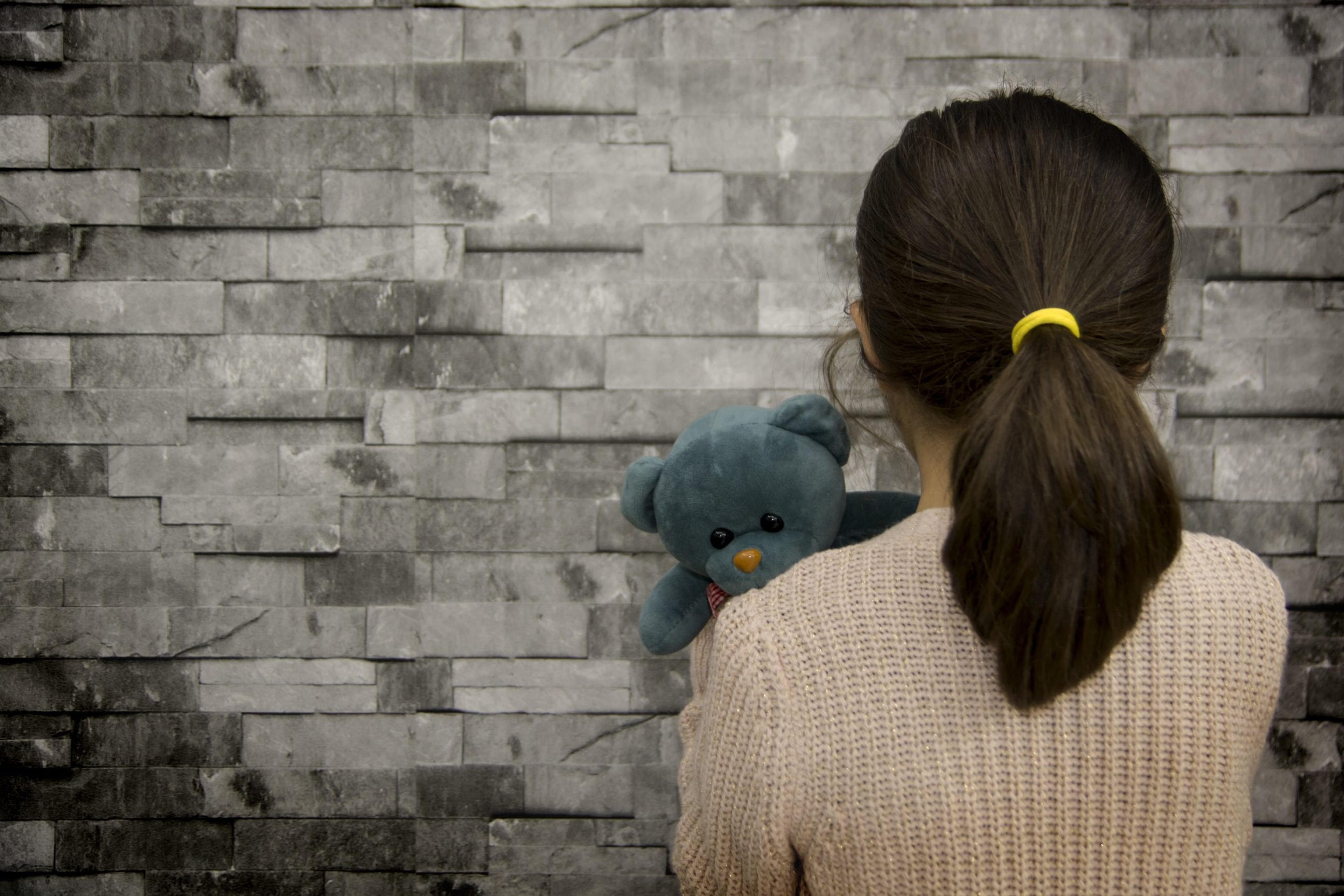 Little girl holding teddy bear with back to camera.