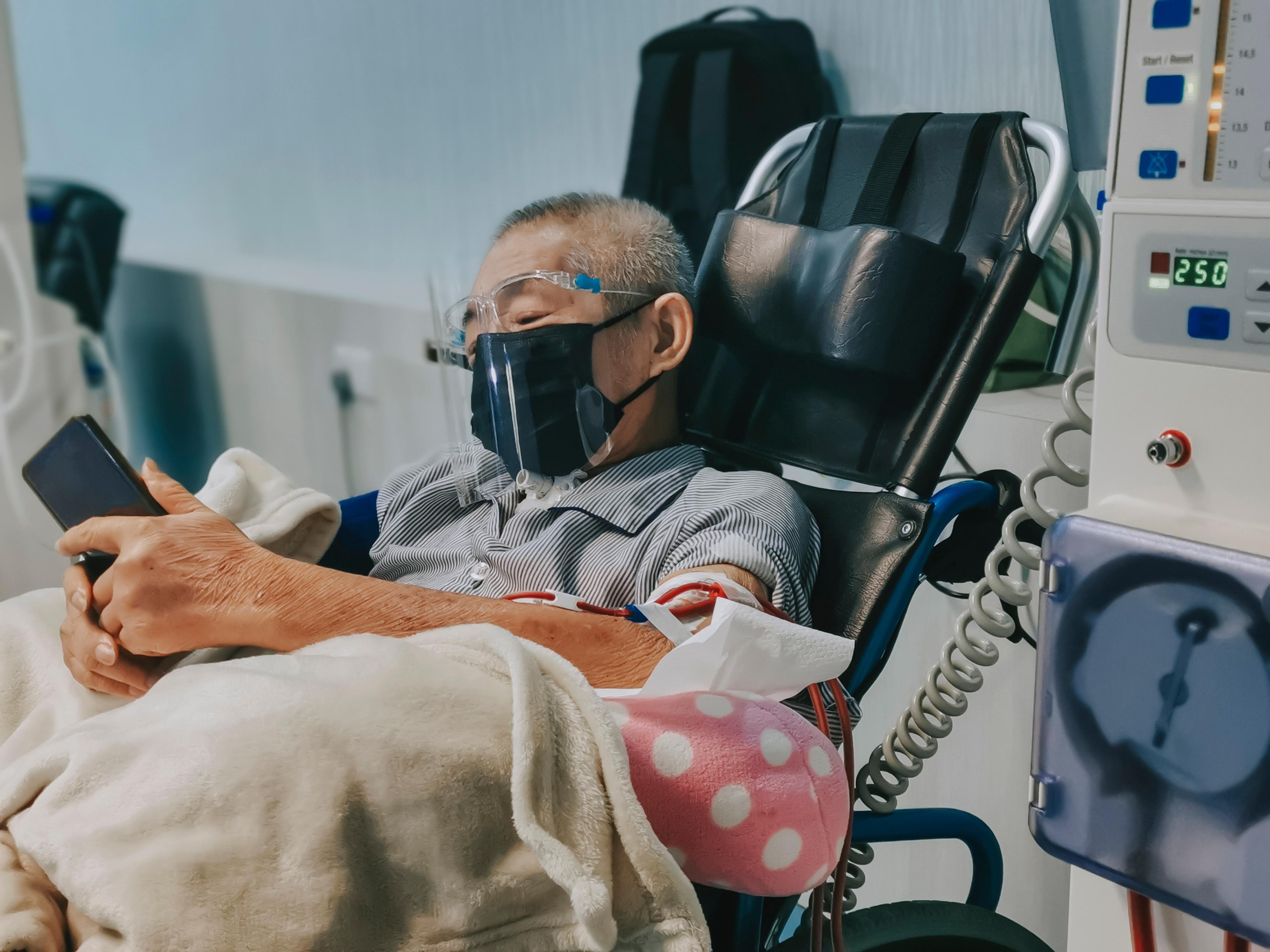 Man in a wheelchair with a mask and face shield receives a medical infusion treatment as he waits for an organ donor