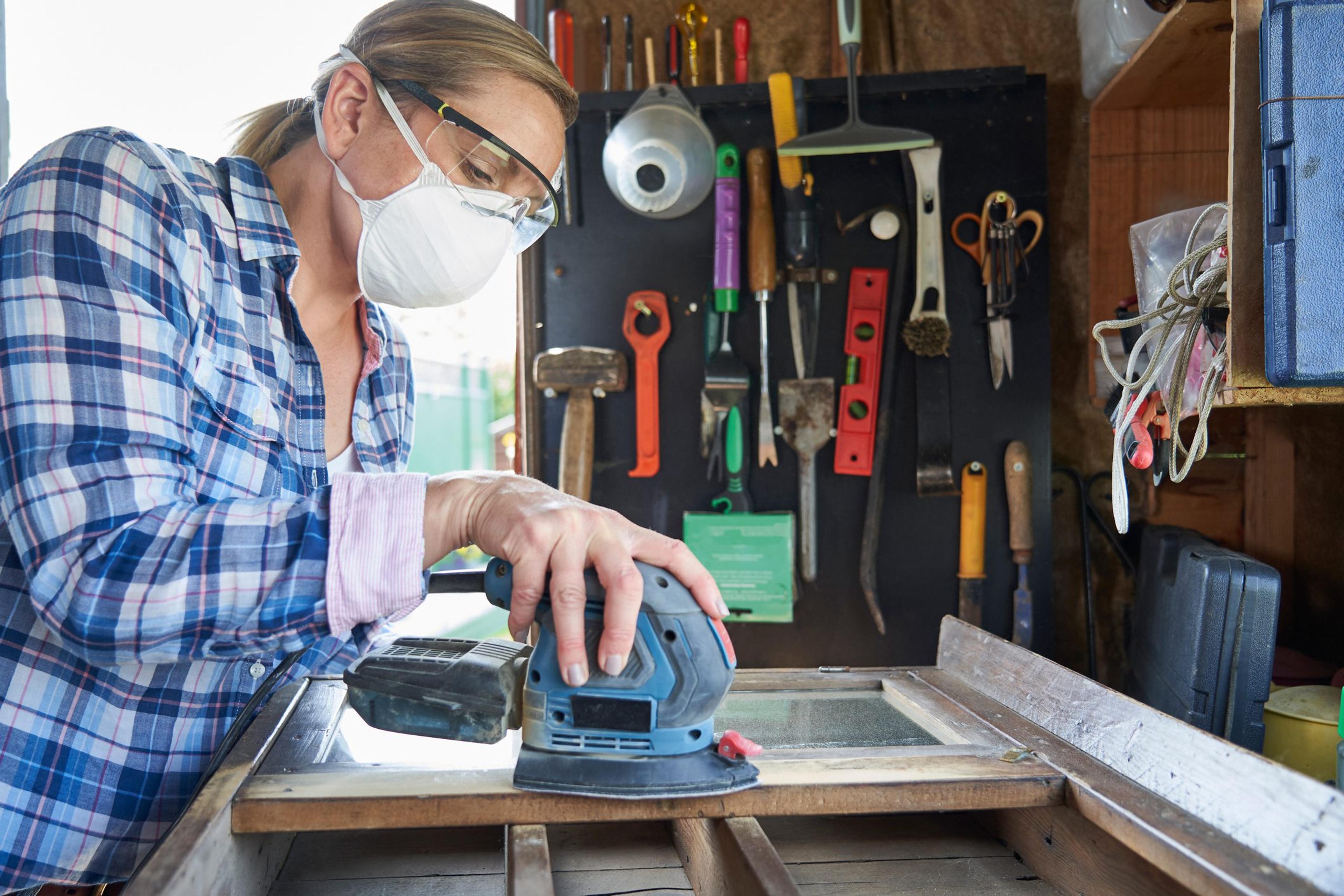 Woman wearing eye protection to avoid common eye injuries sands furniture in her workshop