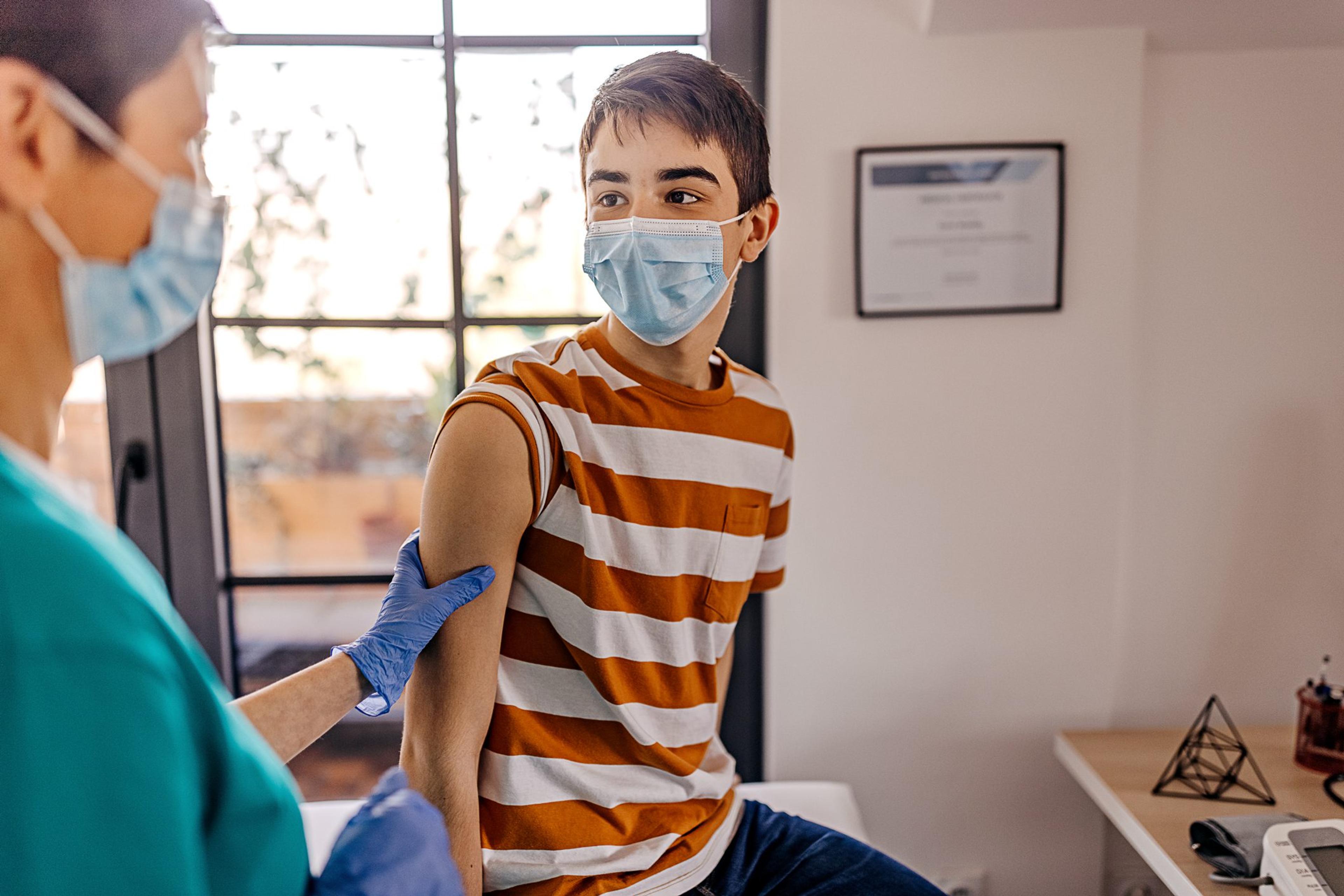 Teenage boy wearing a mask waits for a COVID vaccine